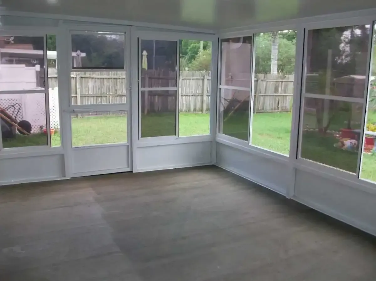 Sunroom with white frames and large windows overlooking a backyard. Empty with gray flooring.
