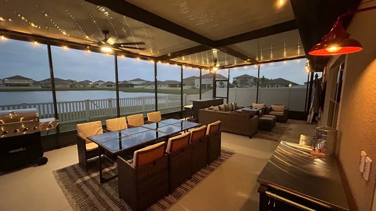 Outdoor screened patio with dining table, seating area, string lights, and a view of a lake.