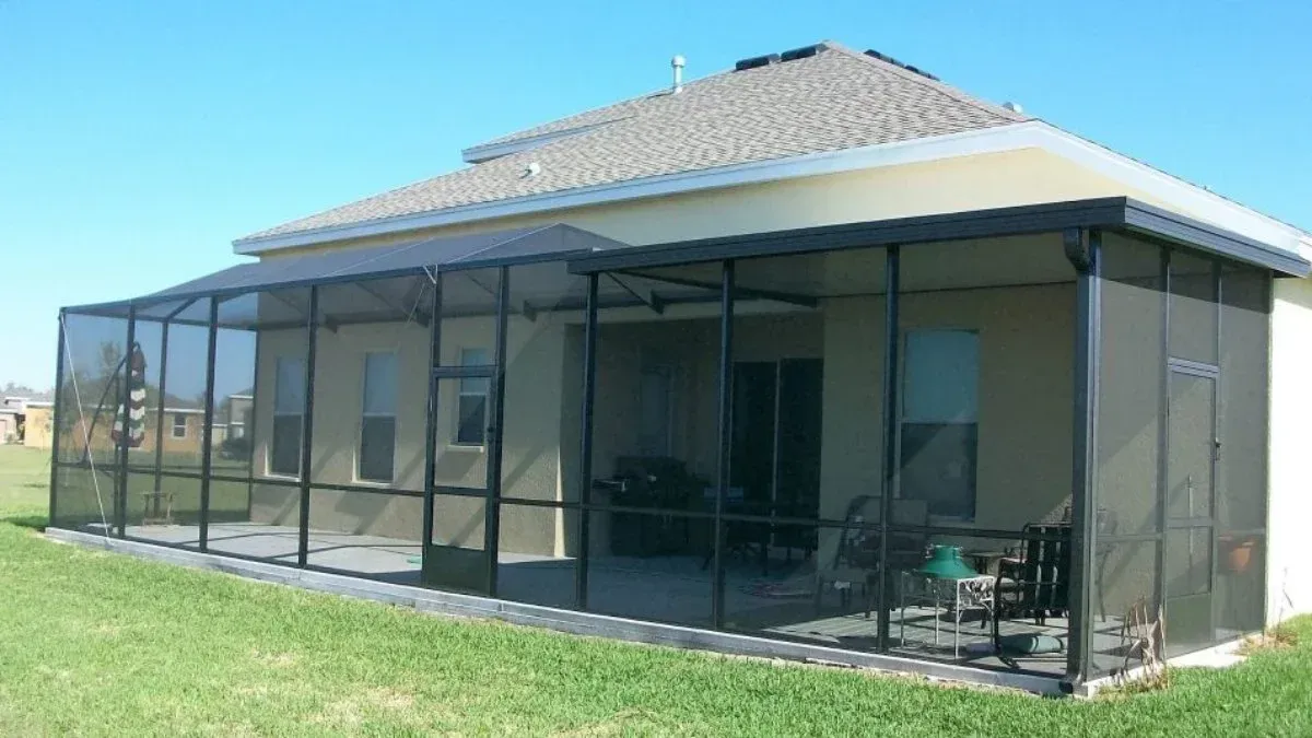 Screened patio enclosure attached to a light-colored house with a dark frame and black screening.