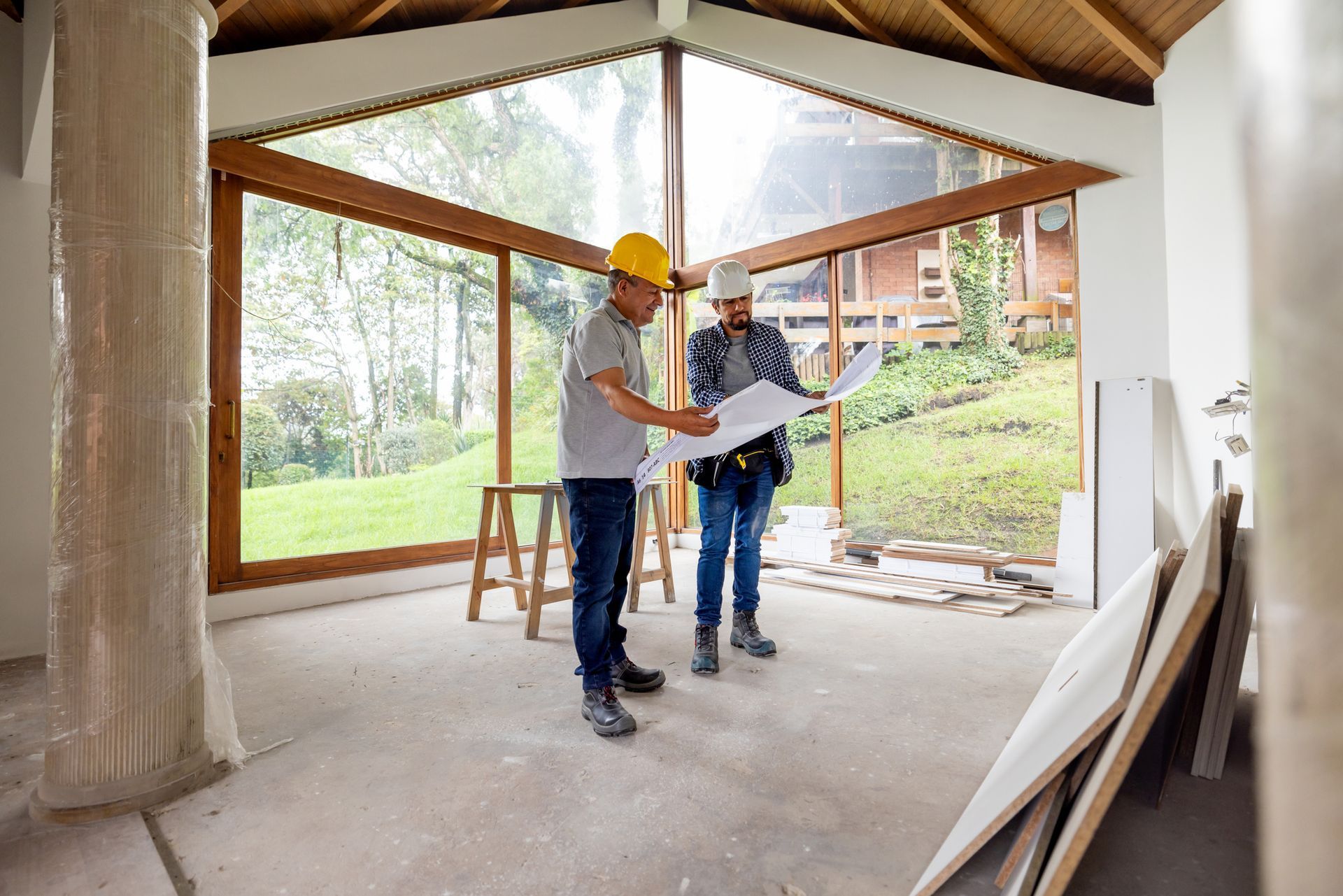 An architect and a construction worker look at a blueprint as they build a patio enclosure.