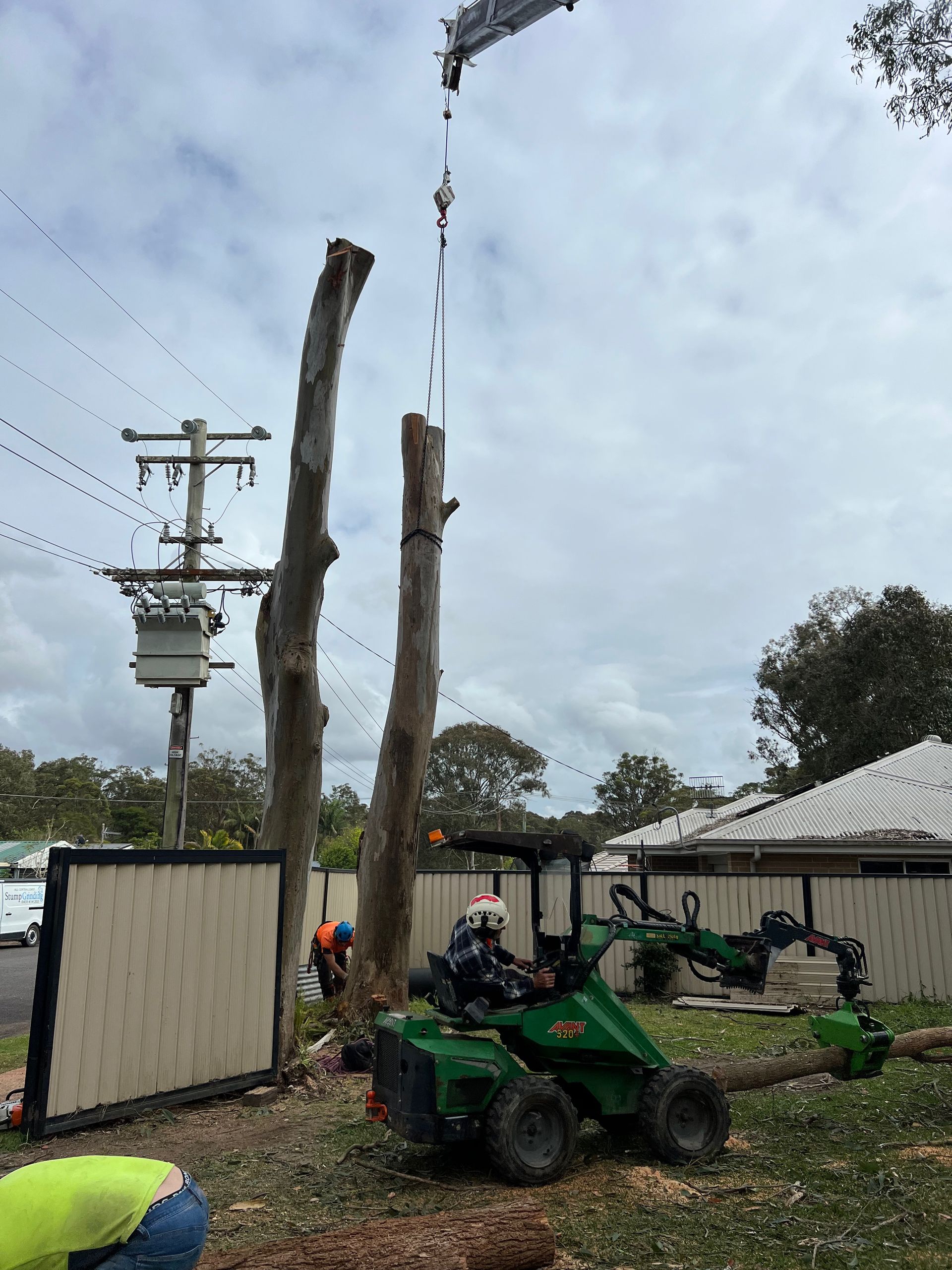 A Tree Stump Grinder Is Cutting a Tree Stump in Front of A House — Central Coast Tree Removal In Budgewoi, NSW