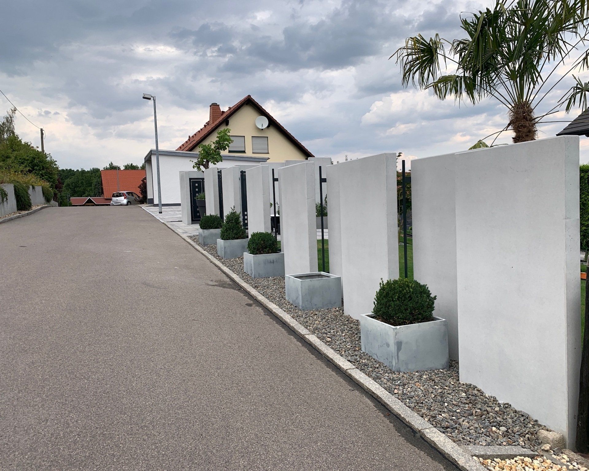 L-Betonsteine in betongrau entlang einer Straße. Im Hintergrund erkennt man Einfamillienhäuser