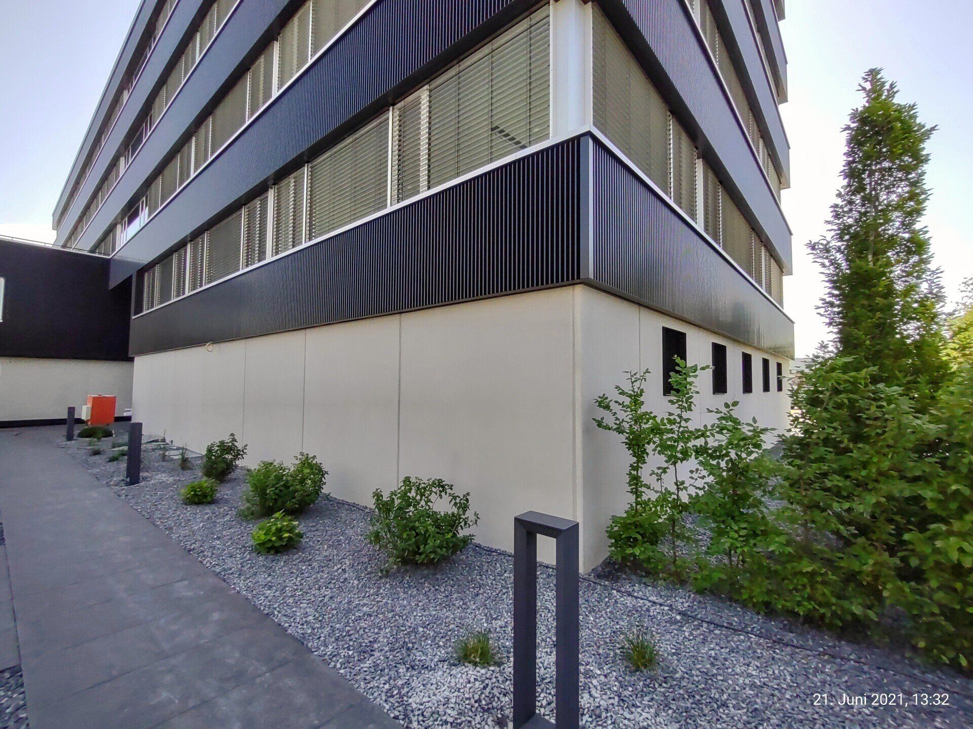 Sichtbeton Kosmetik an einer Feng Shui Haus Fassade von rauMKult Sichtbeton, oberhalb des Betons sind schwarze Fassaden Elemente und davor stehen im Kies grüne Sträucher