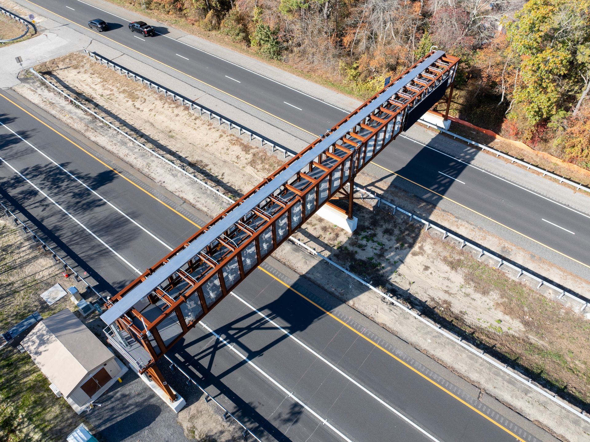 Aerial view of a weathered brown steel bridge structure crossing over a multi-lane highway with passing vehicles.