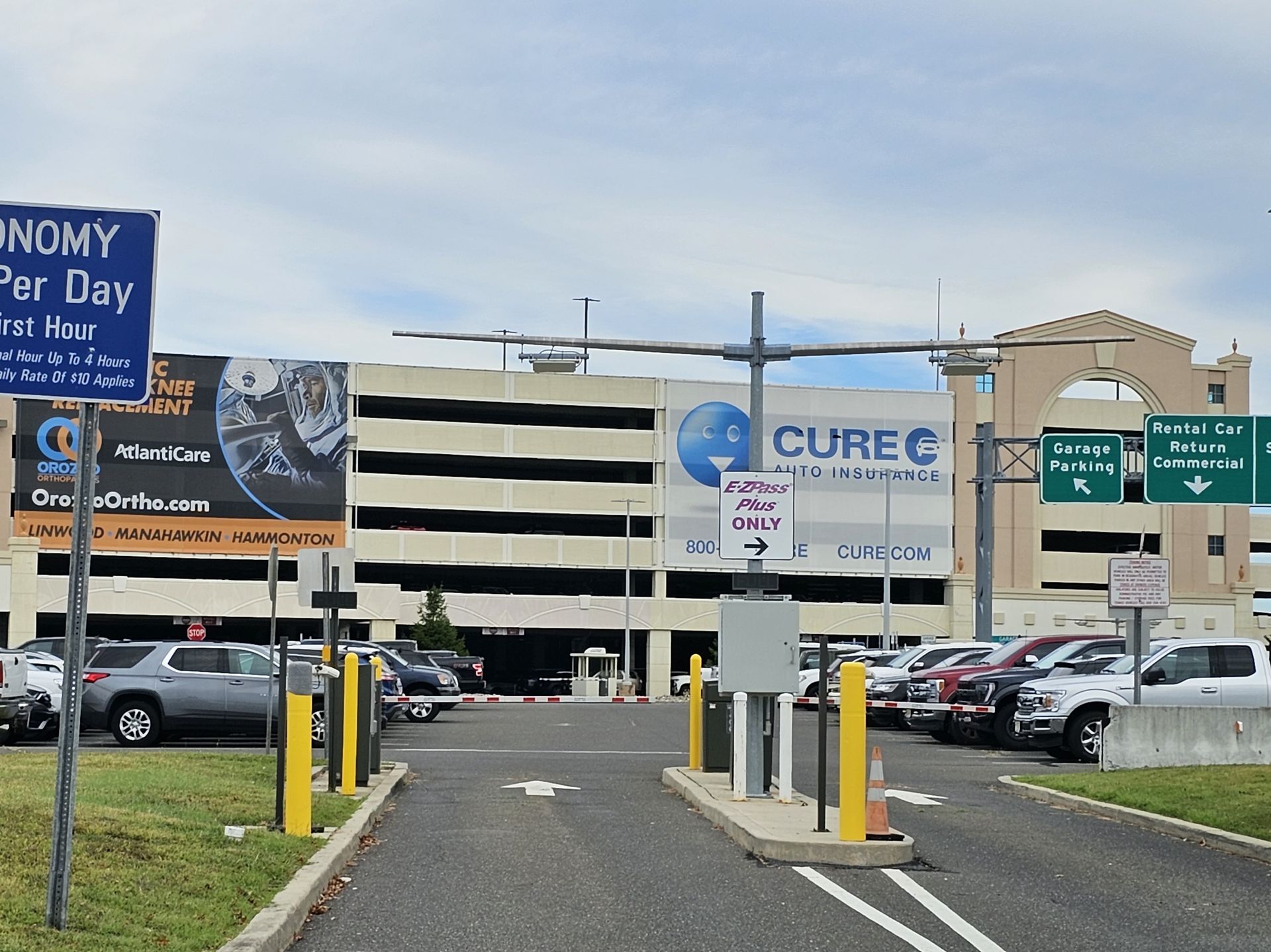 Entrance to a multistory parking garage with cars, directional signage, and a large Cure Auto Insurance advertisement.