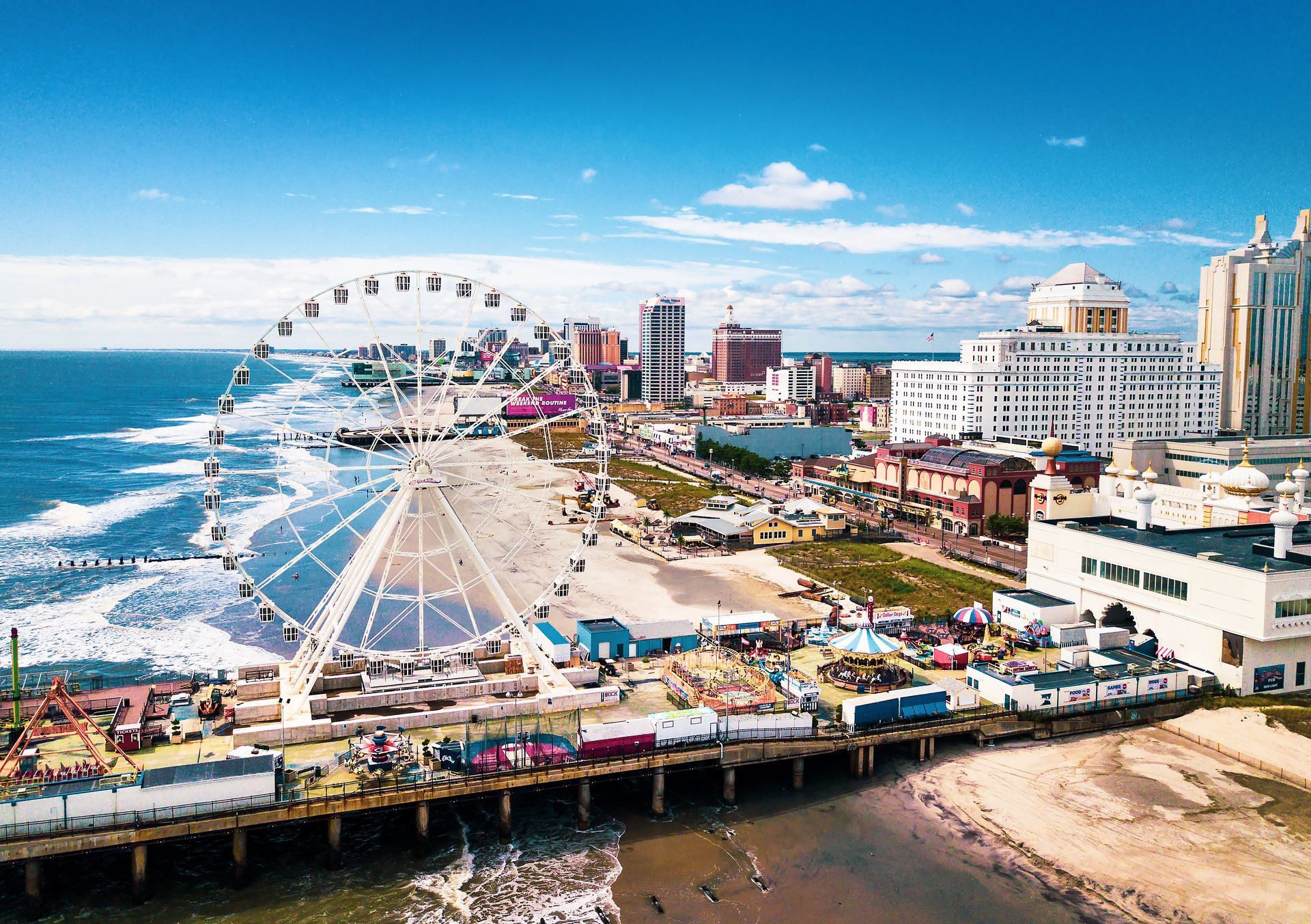 An aerial view of the Atlantic City Boardwalk, featuring a large Ferris wheel, sandy beach, and city skyline.