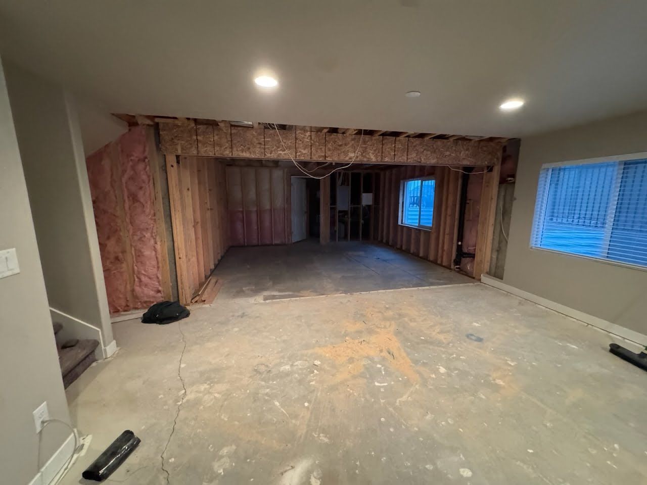 Partially finished basement room with exposed pink insulation and concrete floor under recessed lights