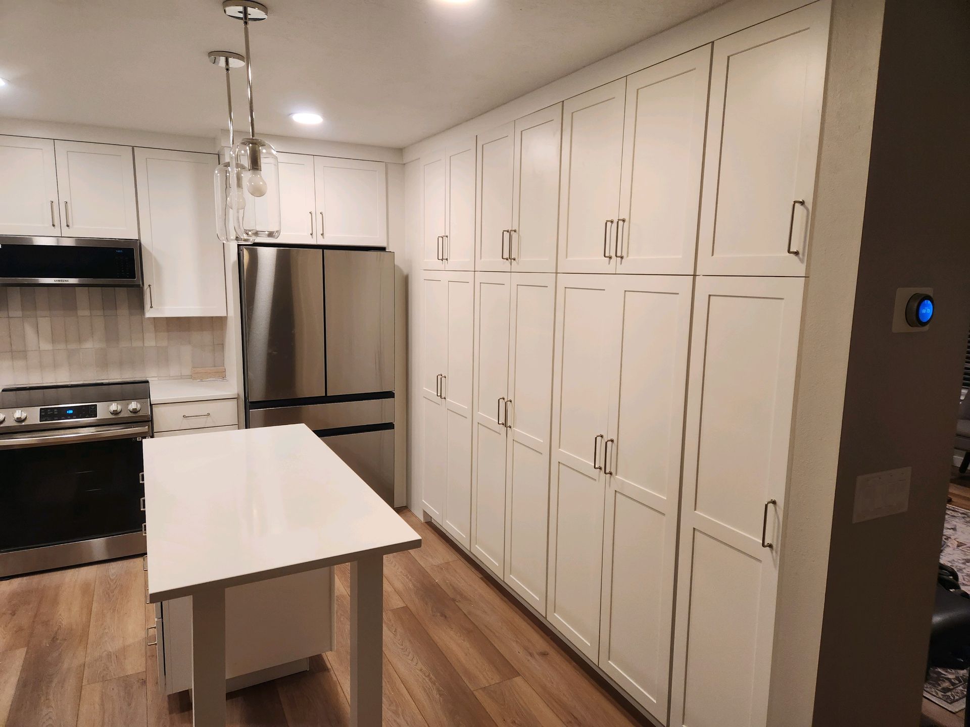 Modern white kitchen with island, stainless steel fridge, stove, and wall of cabinets