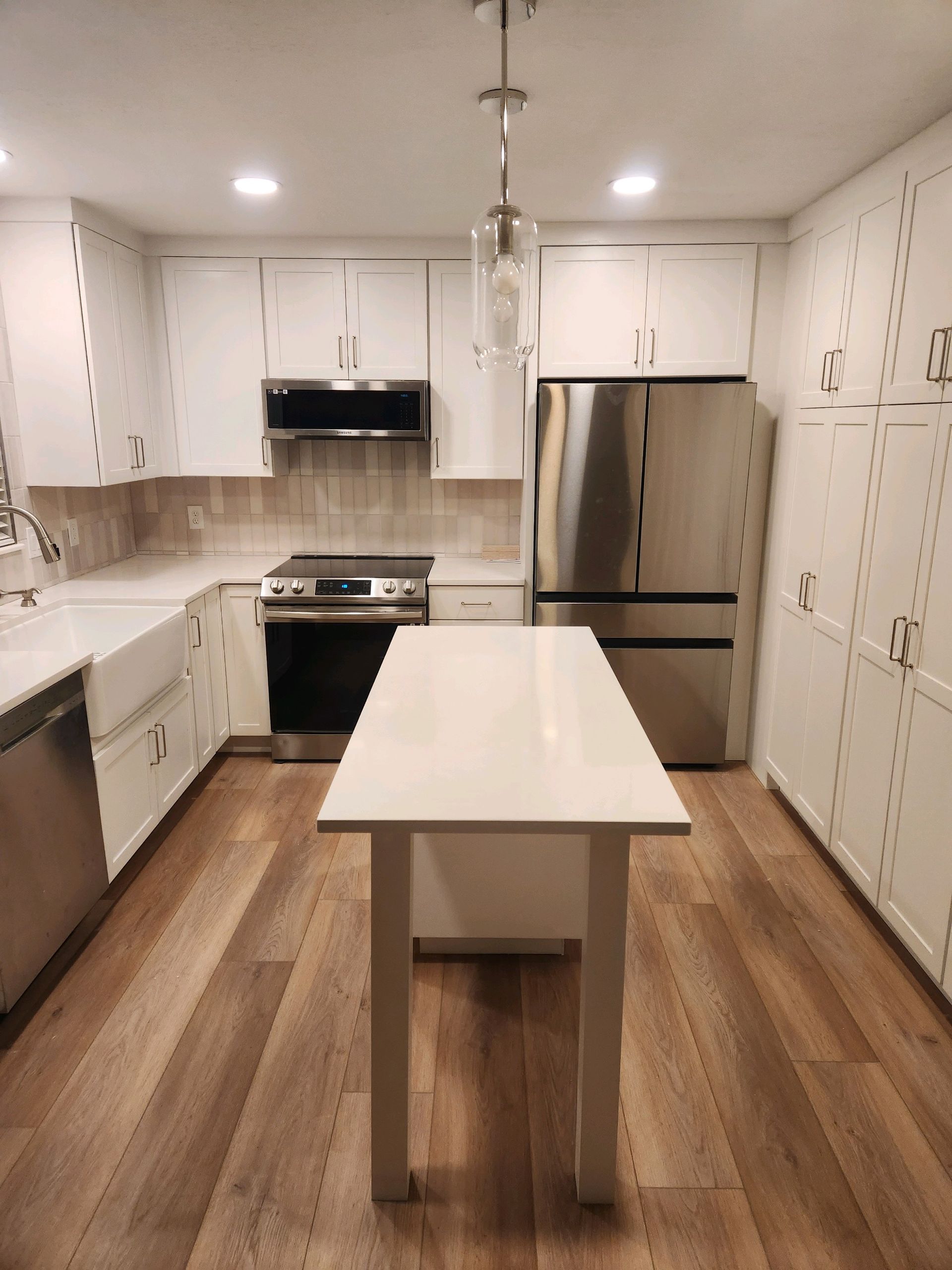 Bright modern kitchen with white cabinets, stainless steel appliances, and a white island table with wooden legs.