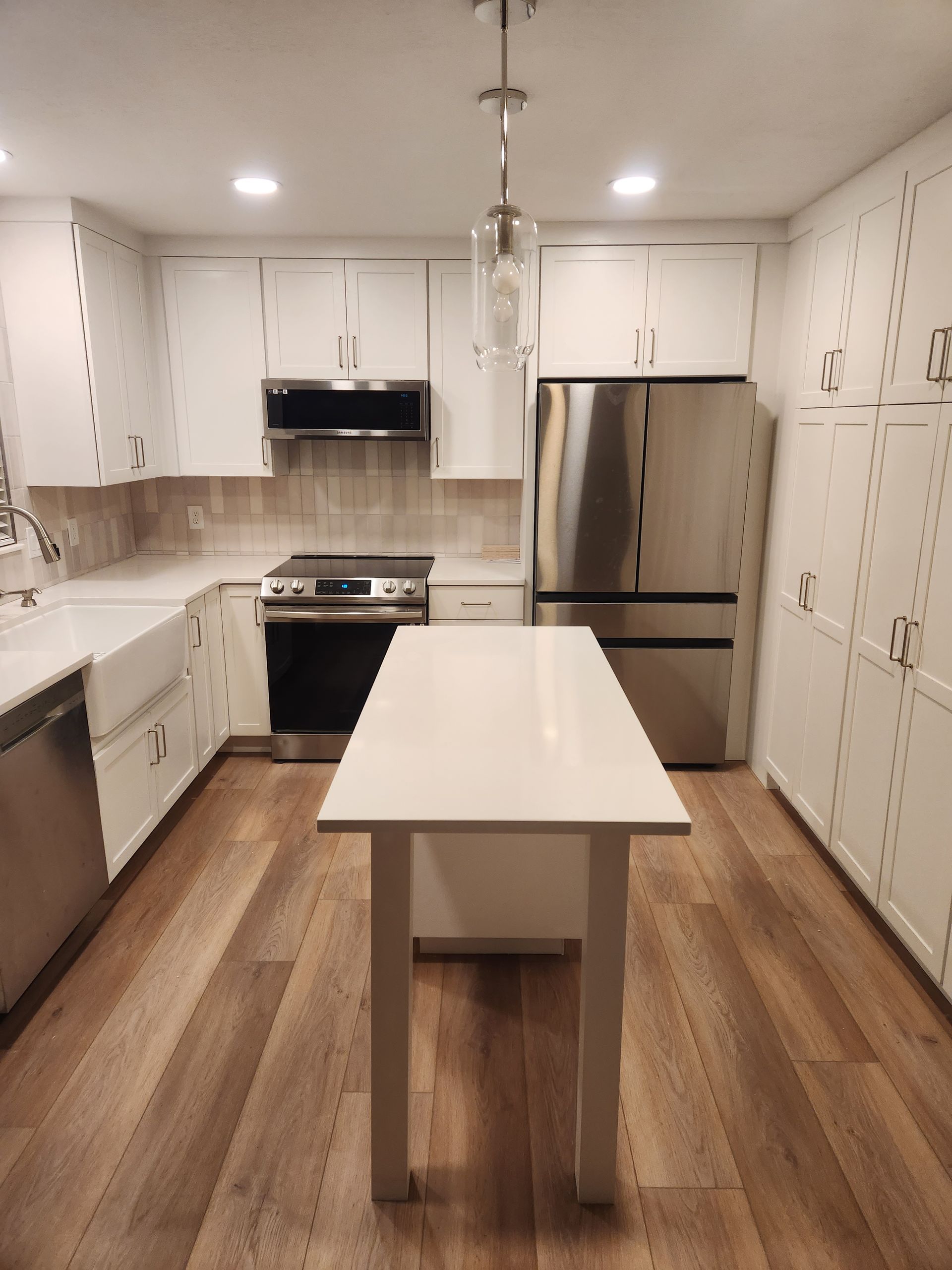 Modern white kitchen with stainless appliances, central island, and wood floors