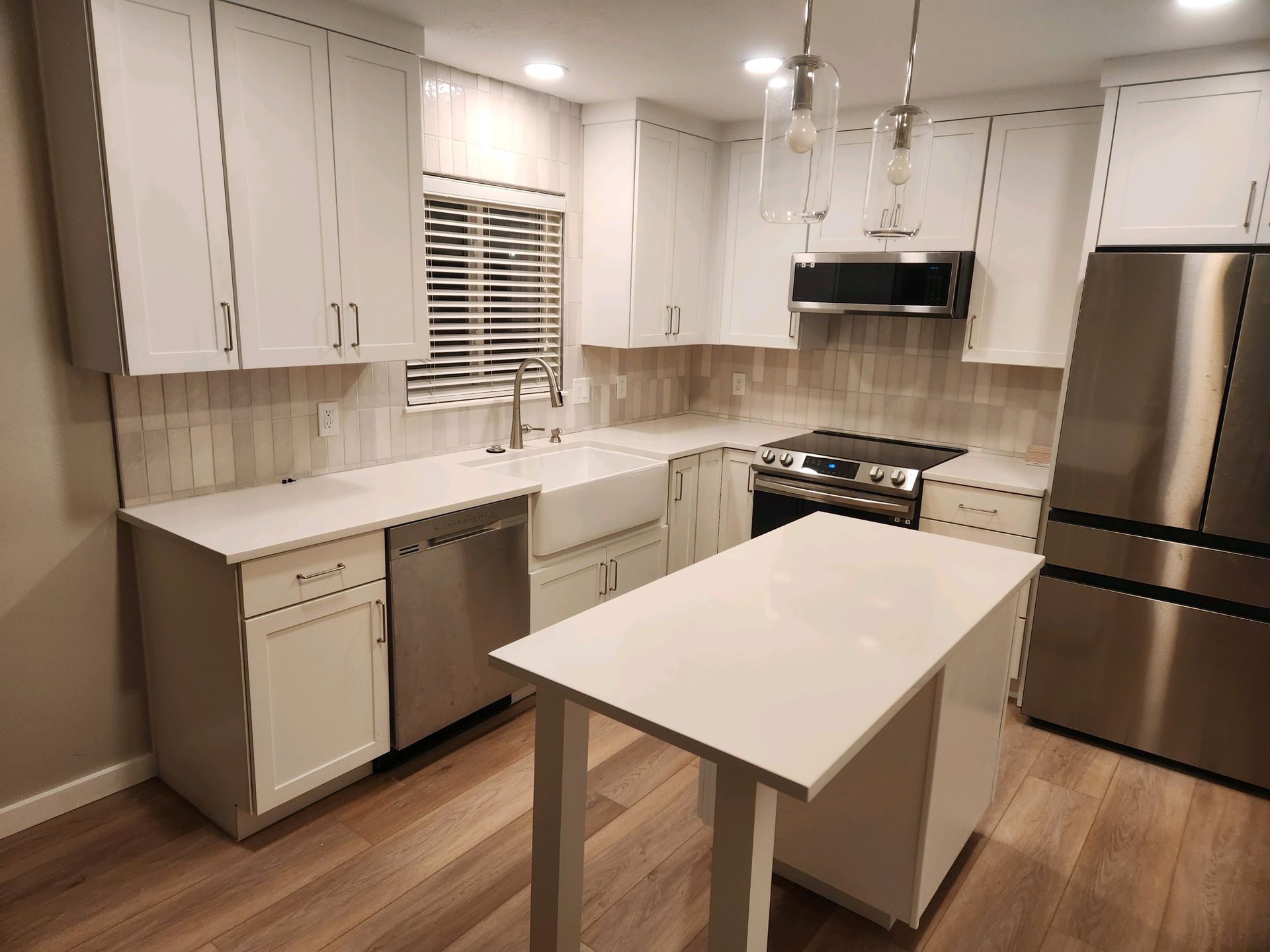 Modern white kitchen with stainless steel appliances, island, and wood floors