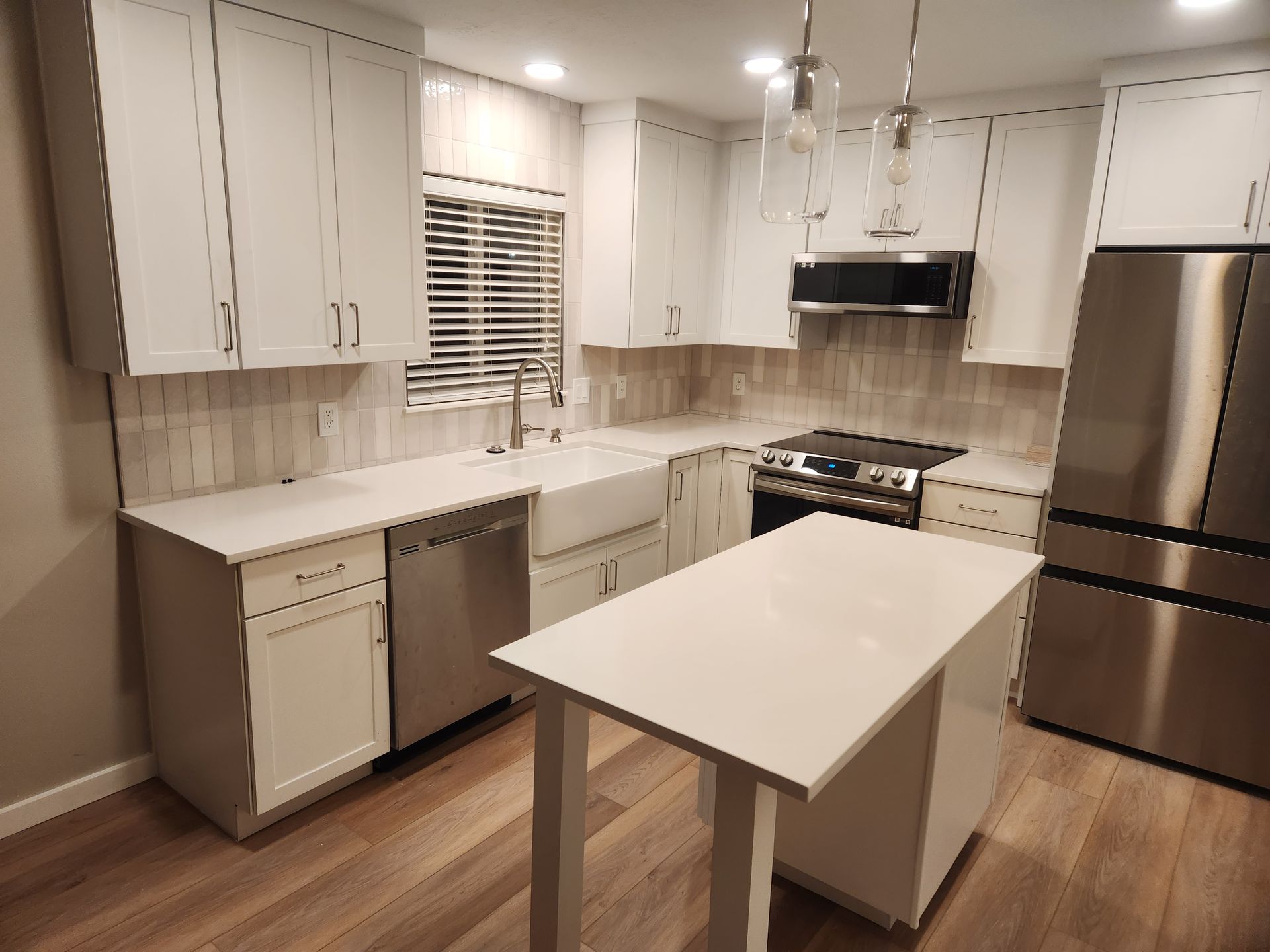 Modern white kitchen with stainless appliances, island, and wood flooring