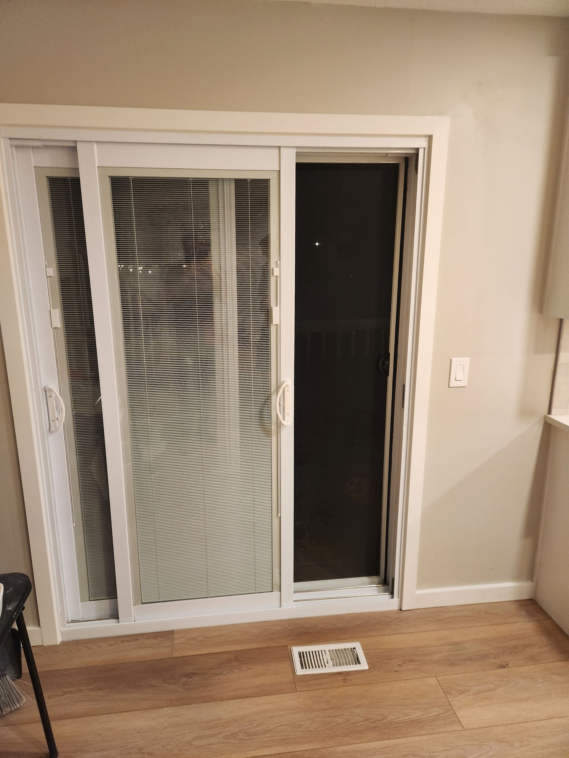 Sliding glass door with white blinds, beige walls, wood floor, and a floor vent in front