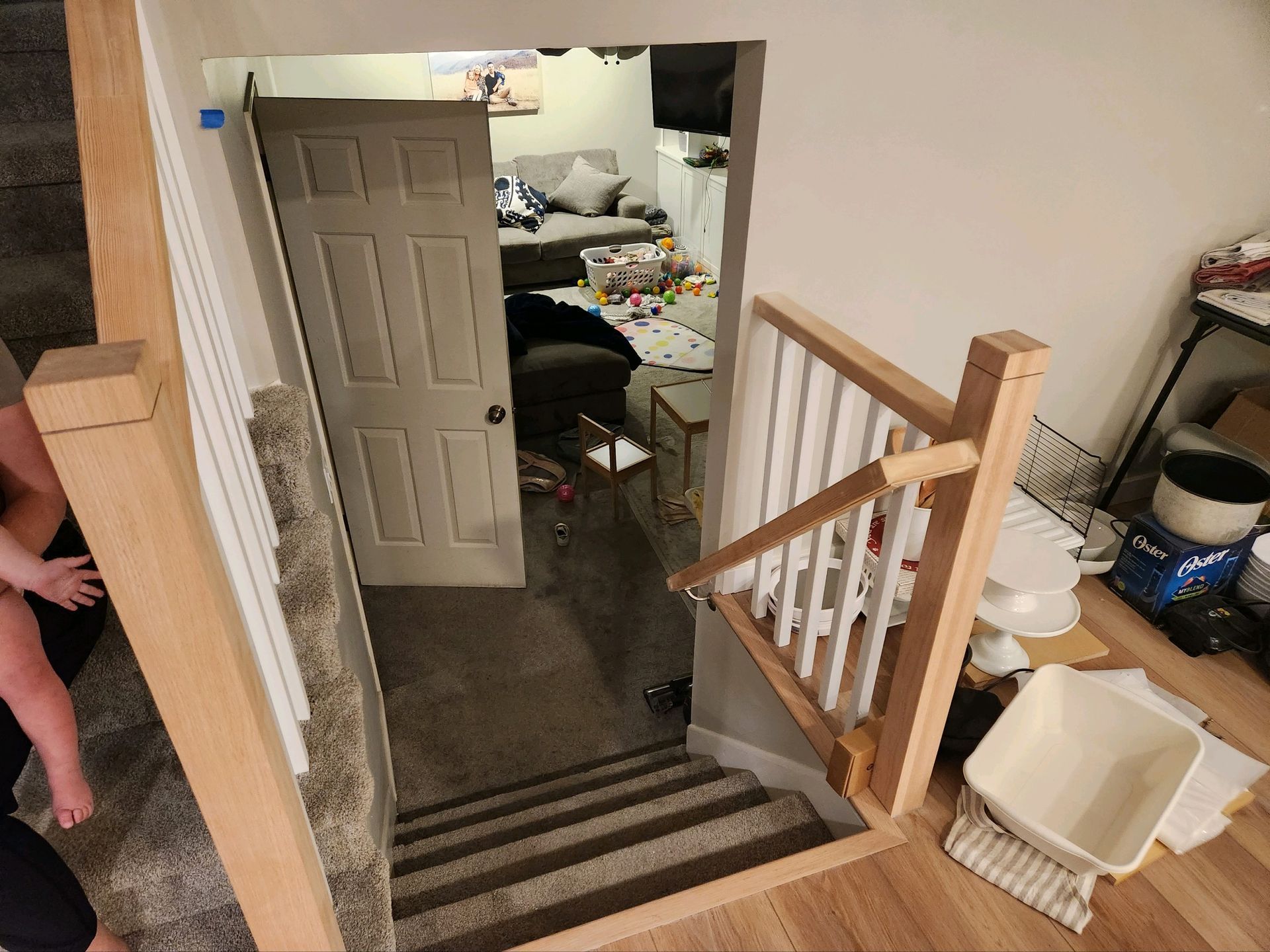 Open doorway at top of stairs into a cluttered room, with wooden railing and a hand on the left.