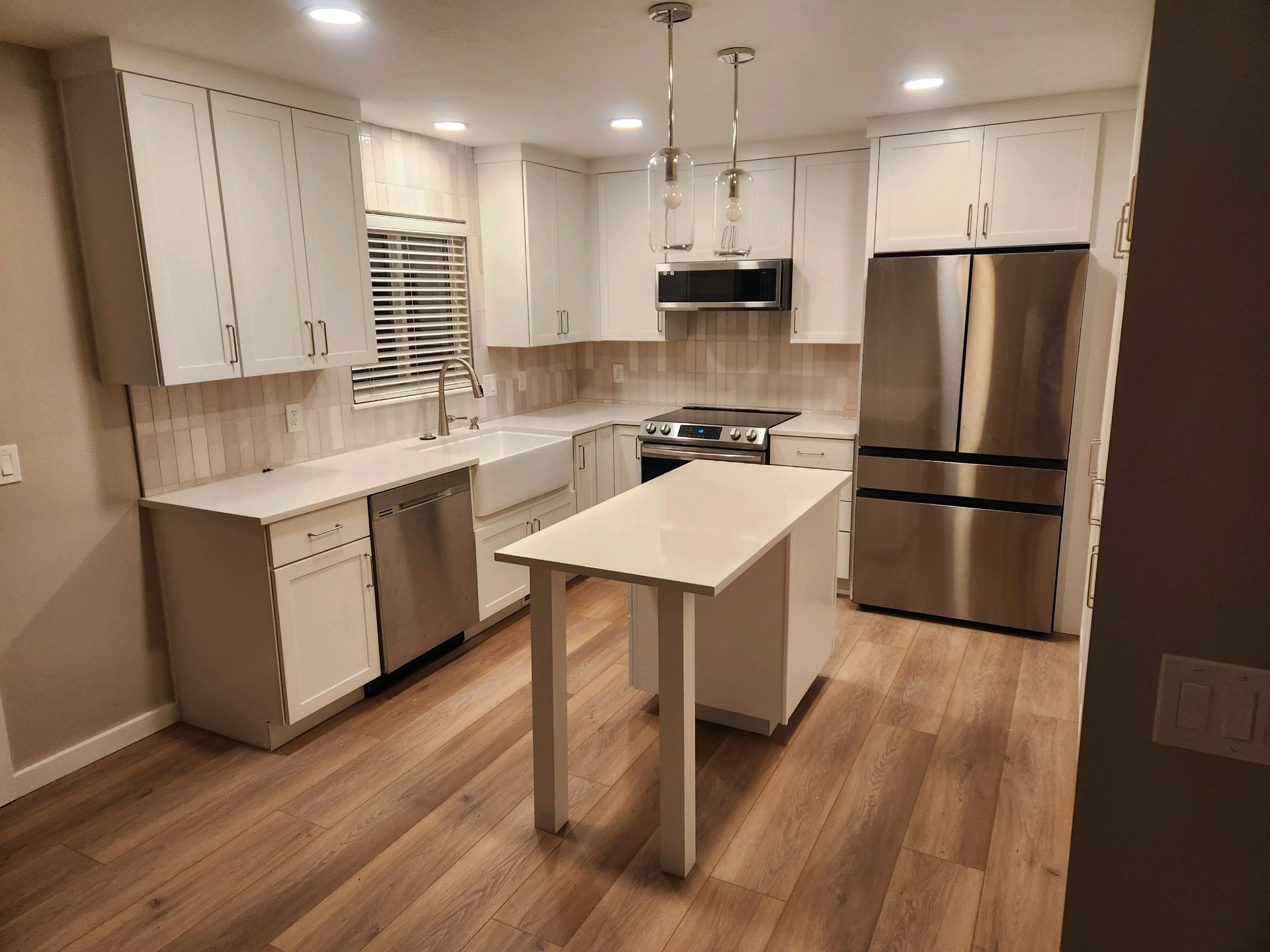Modern white kitchen with stainless steel appliances and a central island on wood floors
