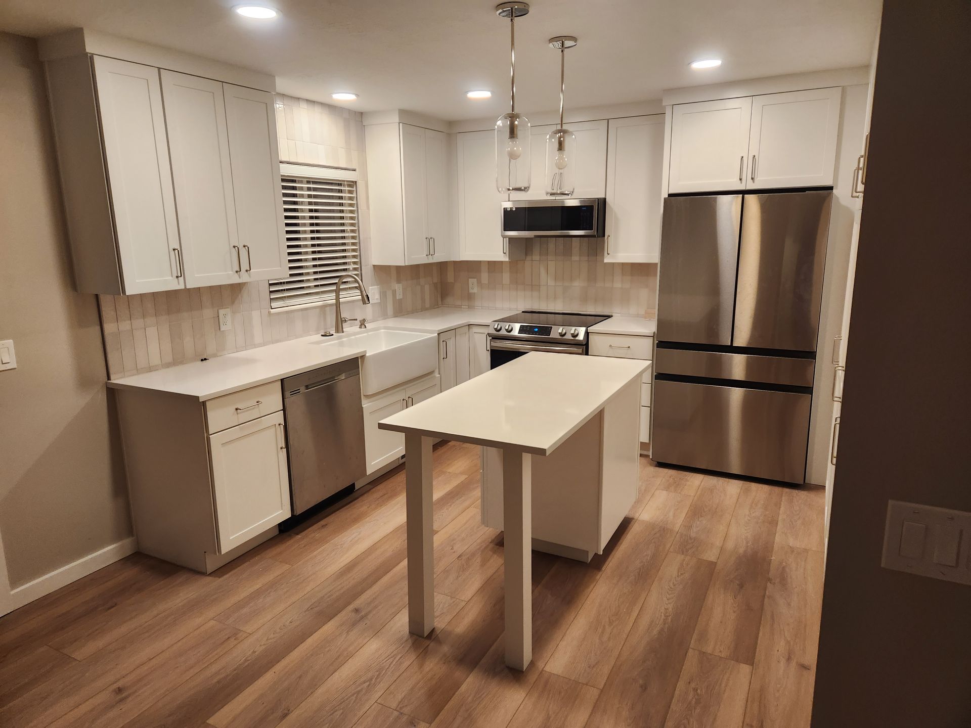 Modern white kitchen with stainless steel appliances, island, and wood floors
