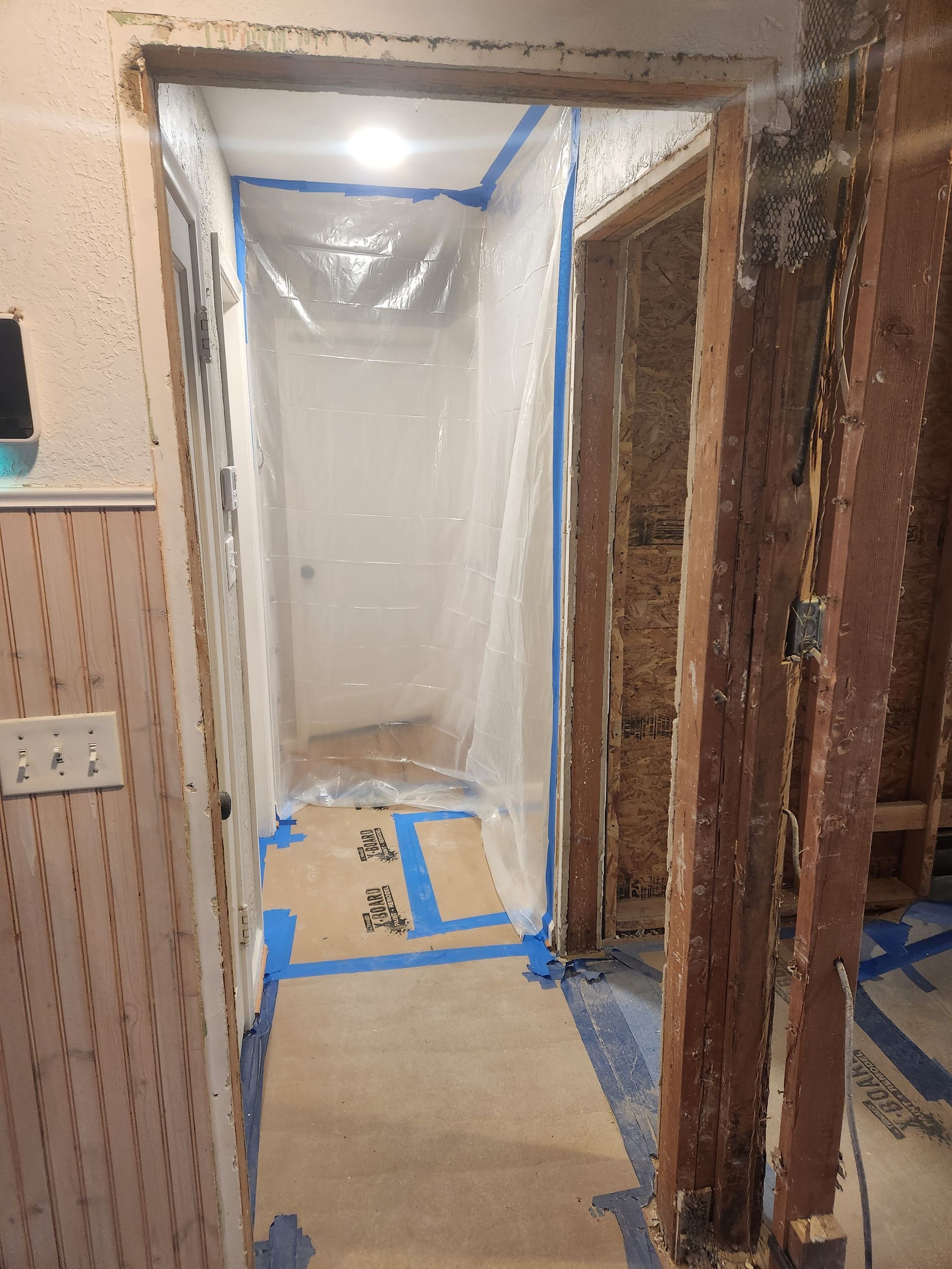 Hallway under renovation, with plastic sheeting covering a doorway and blue painter’s tape on the floor.