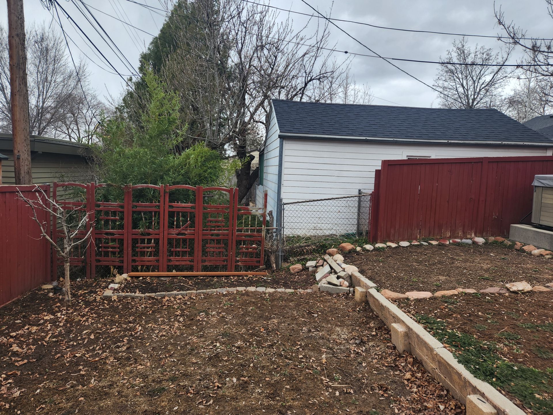 Backyard with red trellis, shed, and leaf-covered ground beside a gravel path