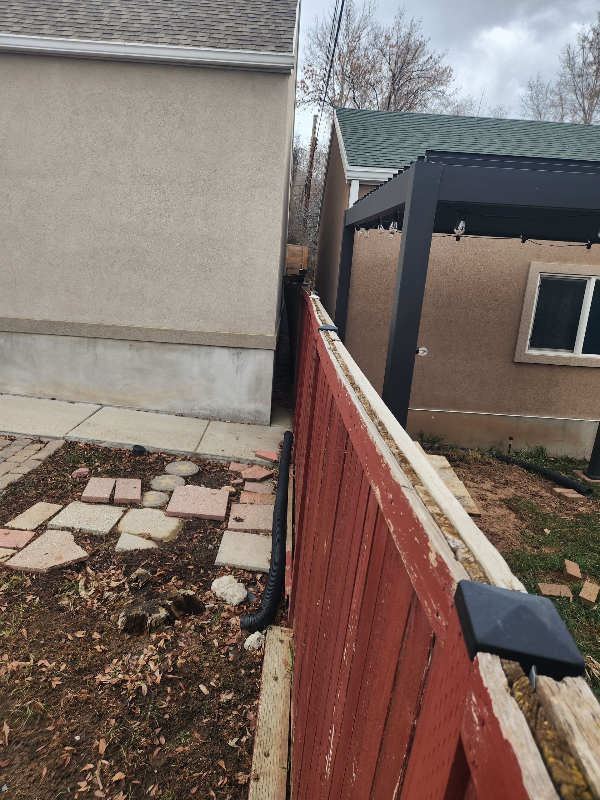 Narrow side yard between buildings with a red wooden fence, stone path, and gravel ground.