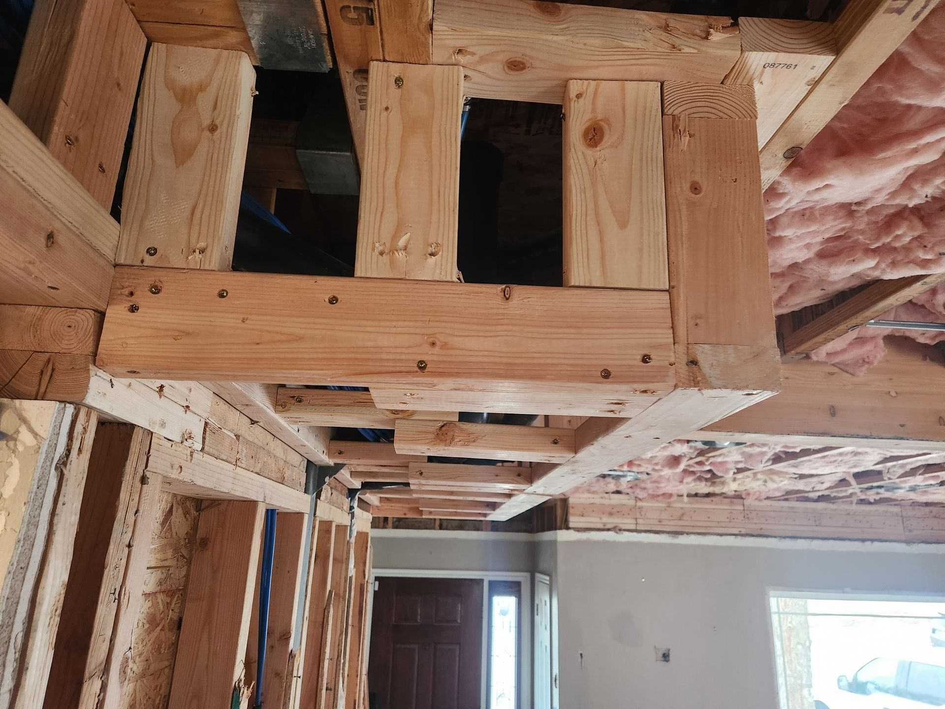 Exposed wooden ceiling framing in an unfinished room with insulation and windows