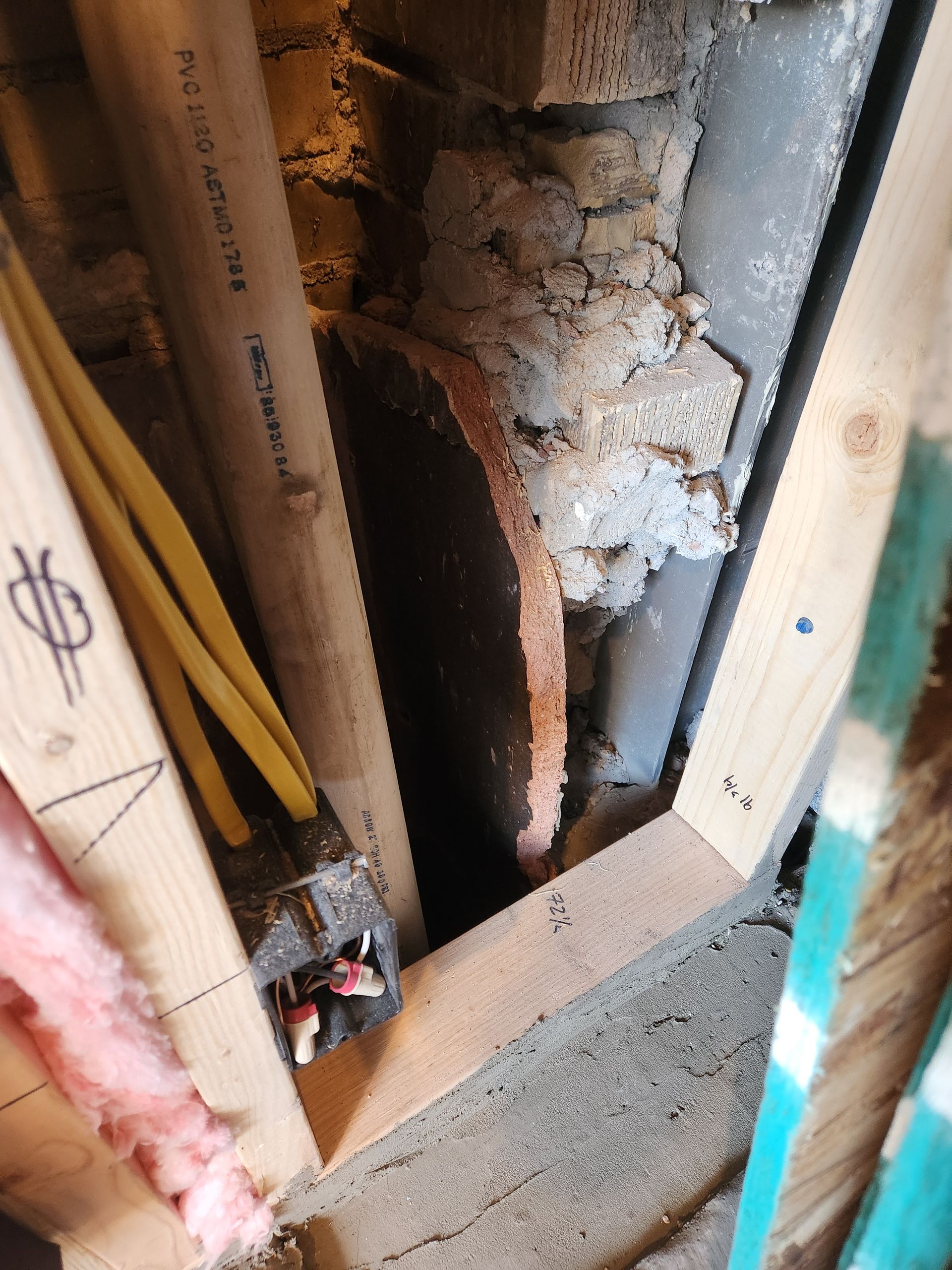 Damaged wall cavity with exposed insulation, wood framing, and debris in a narrow interior space