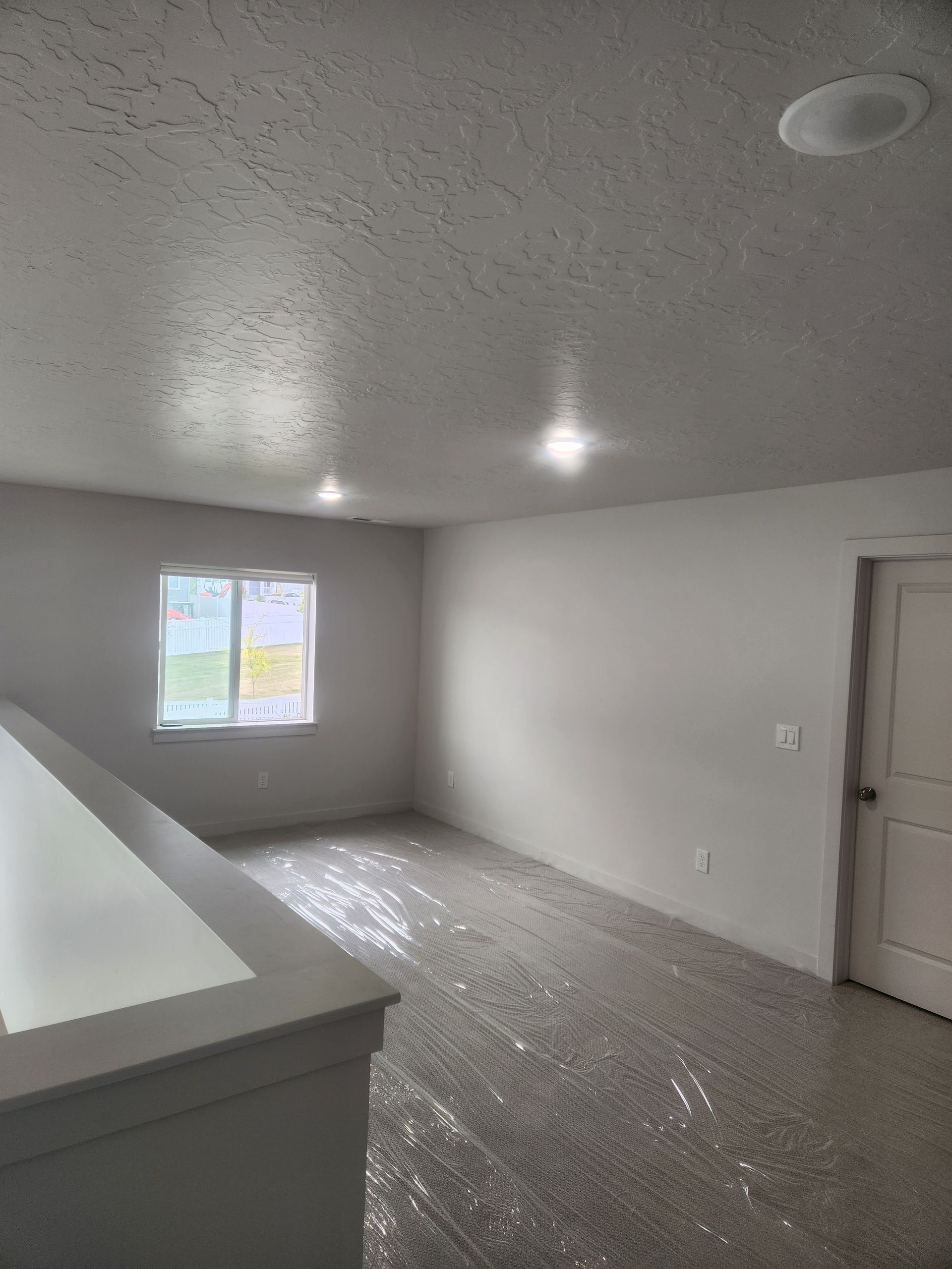 Empty white bedroom with a window, ceiling light, and closet door.