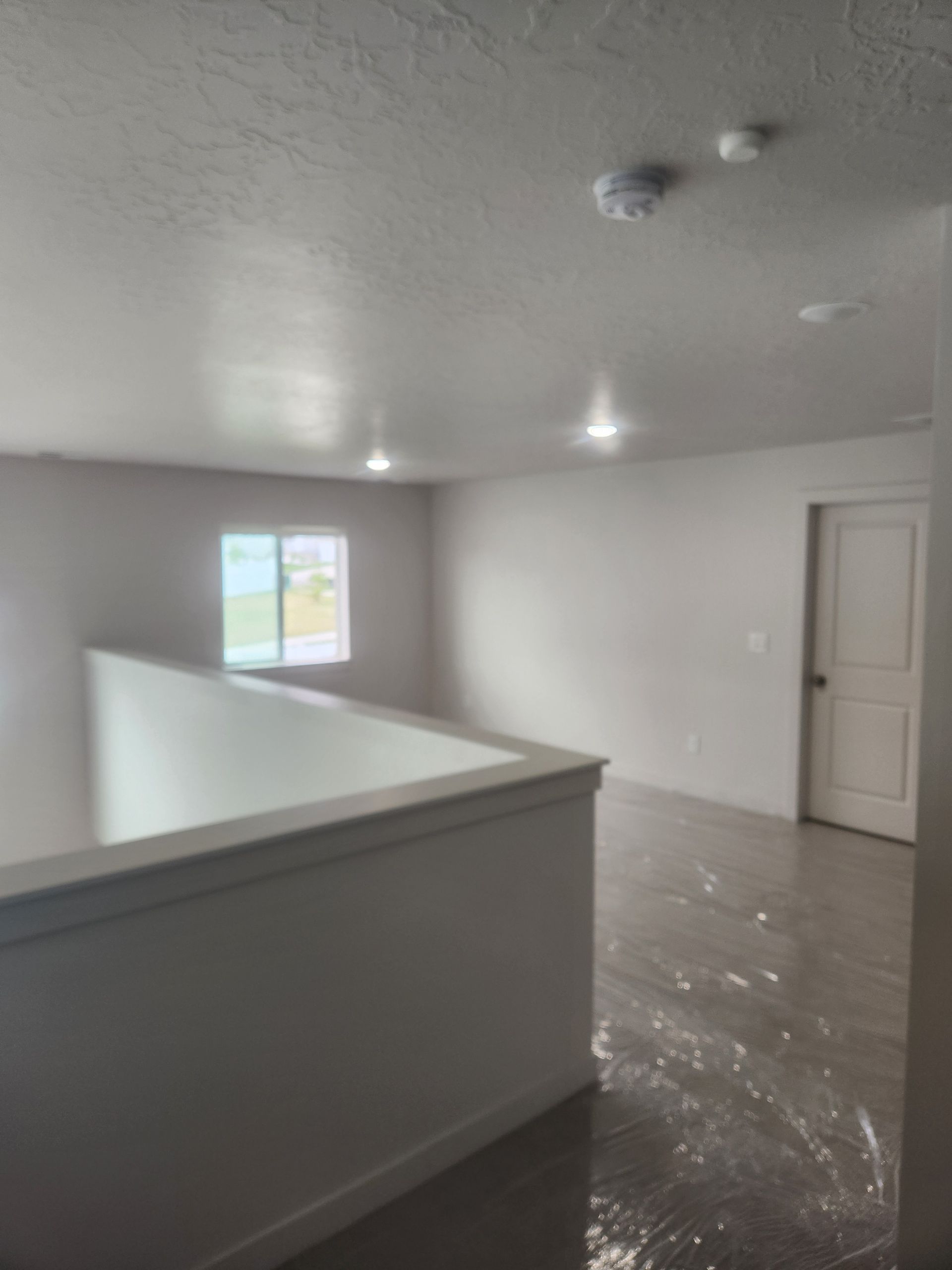 Empty white room with glossy floor, half wall, window, and closed door