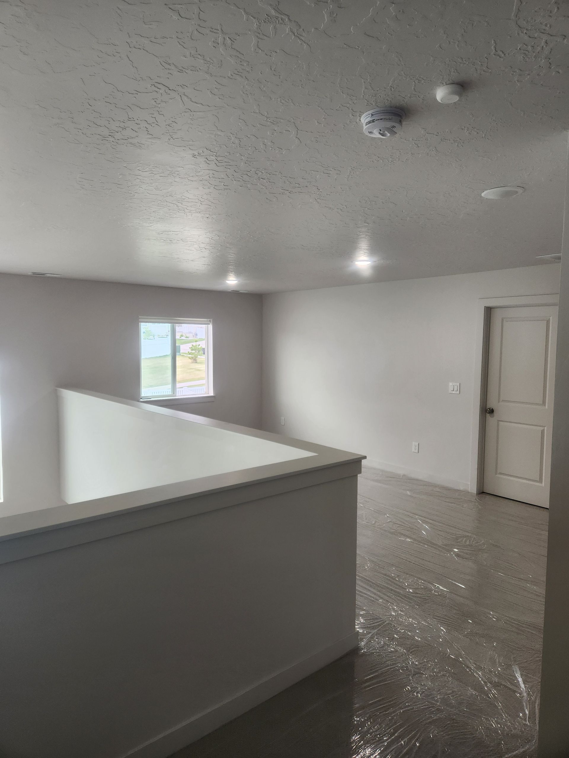 Empty gray upstairs hallway with a half wall, window, white door, and speckled floor.