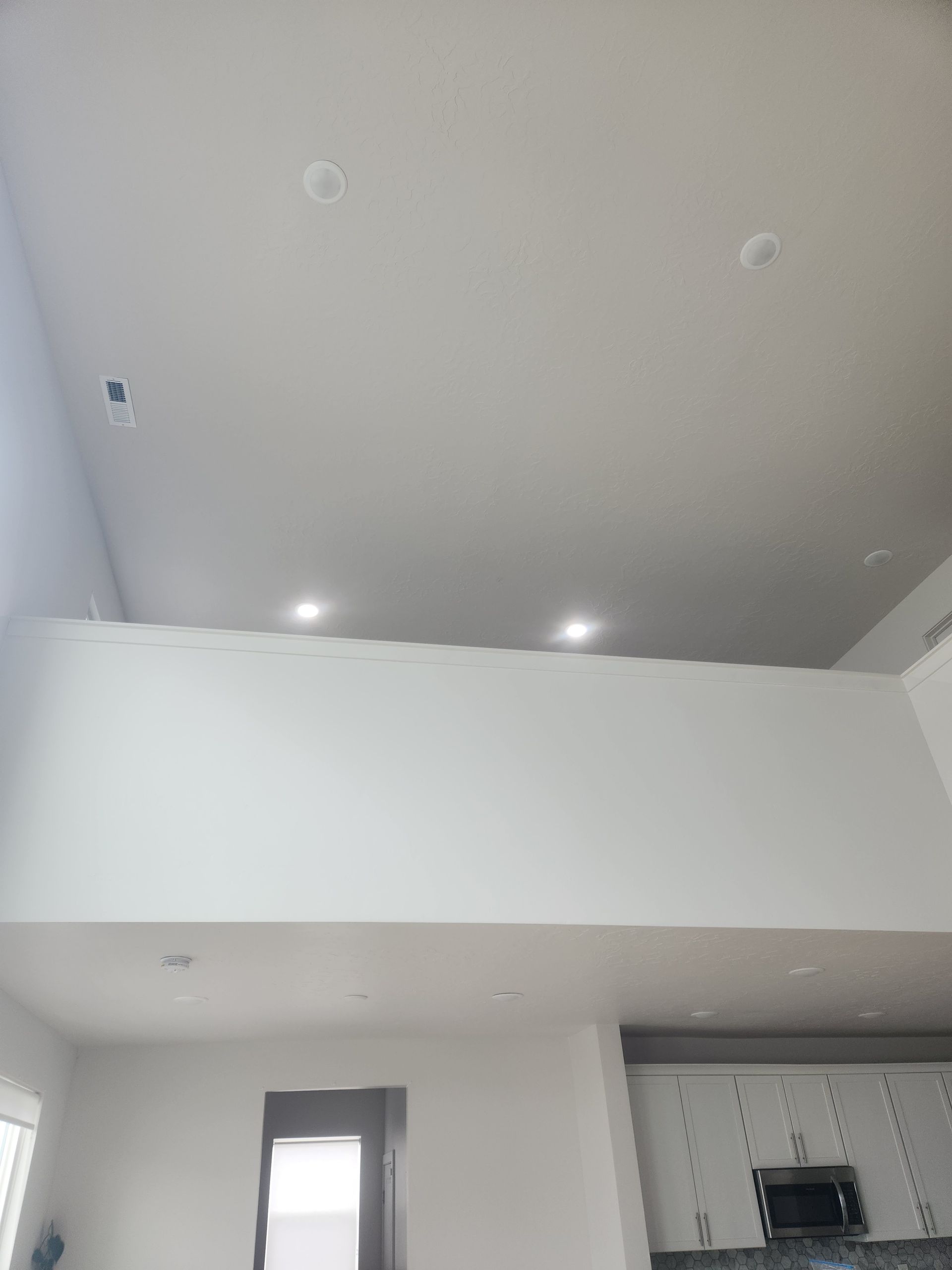 Bright modern living room with high gray ceiling, white walls, recessed lights, and a window.