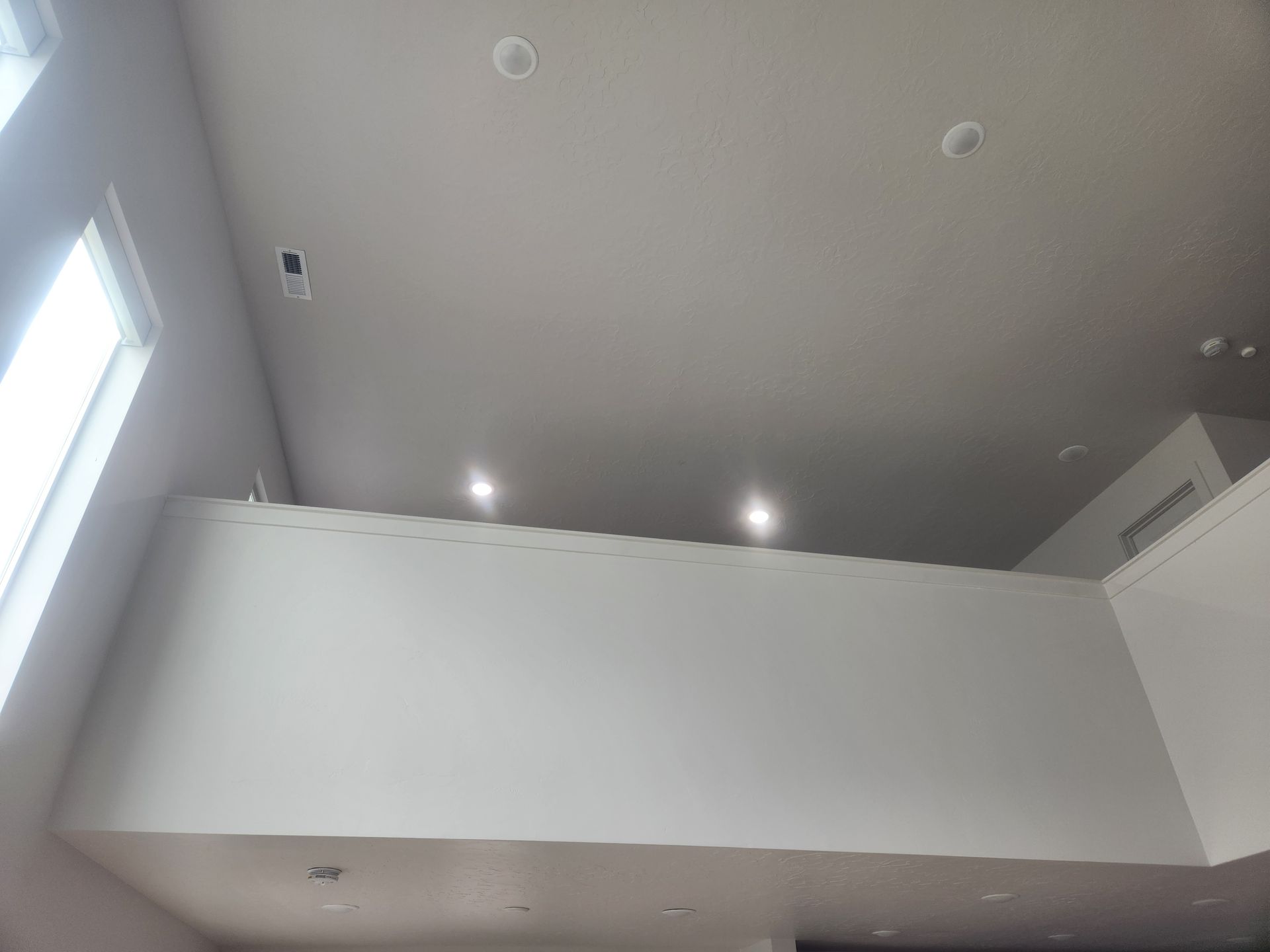 Modern white interior with a high ceiling, recessed lights, and a lofted balcony wall.