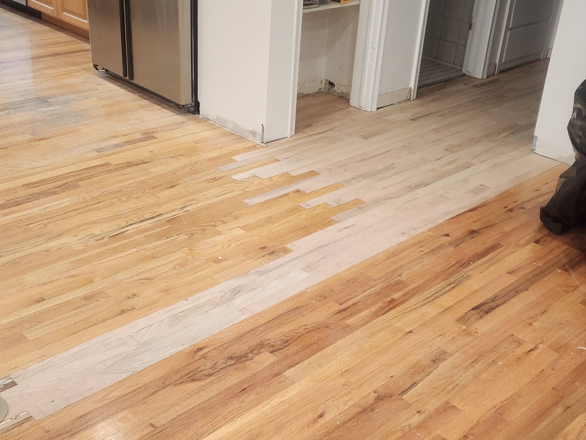 Partially refinished hardwood floor with a lighter unfinished strip in a hallway