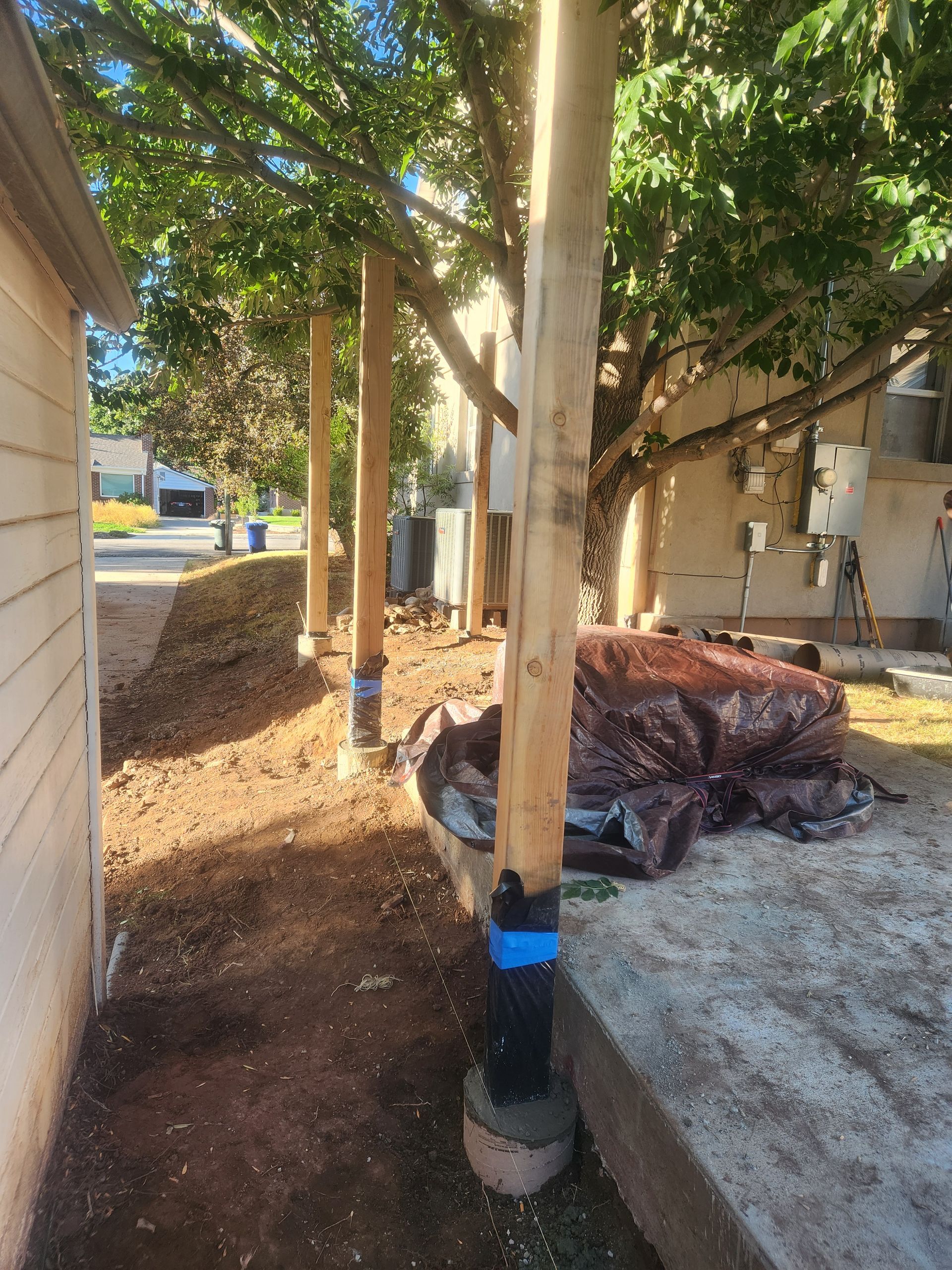 Outdoor walkway beside a building with trees, utility poles, and dirt piles from ongoing landscaping work