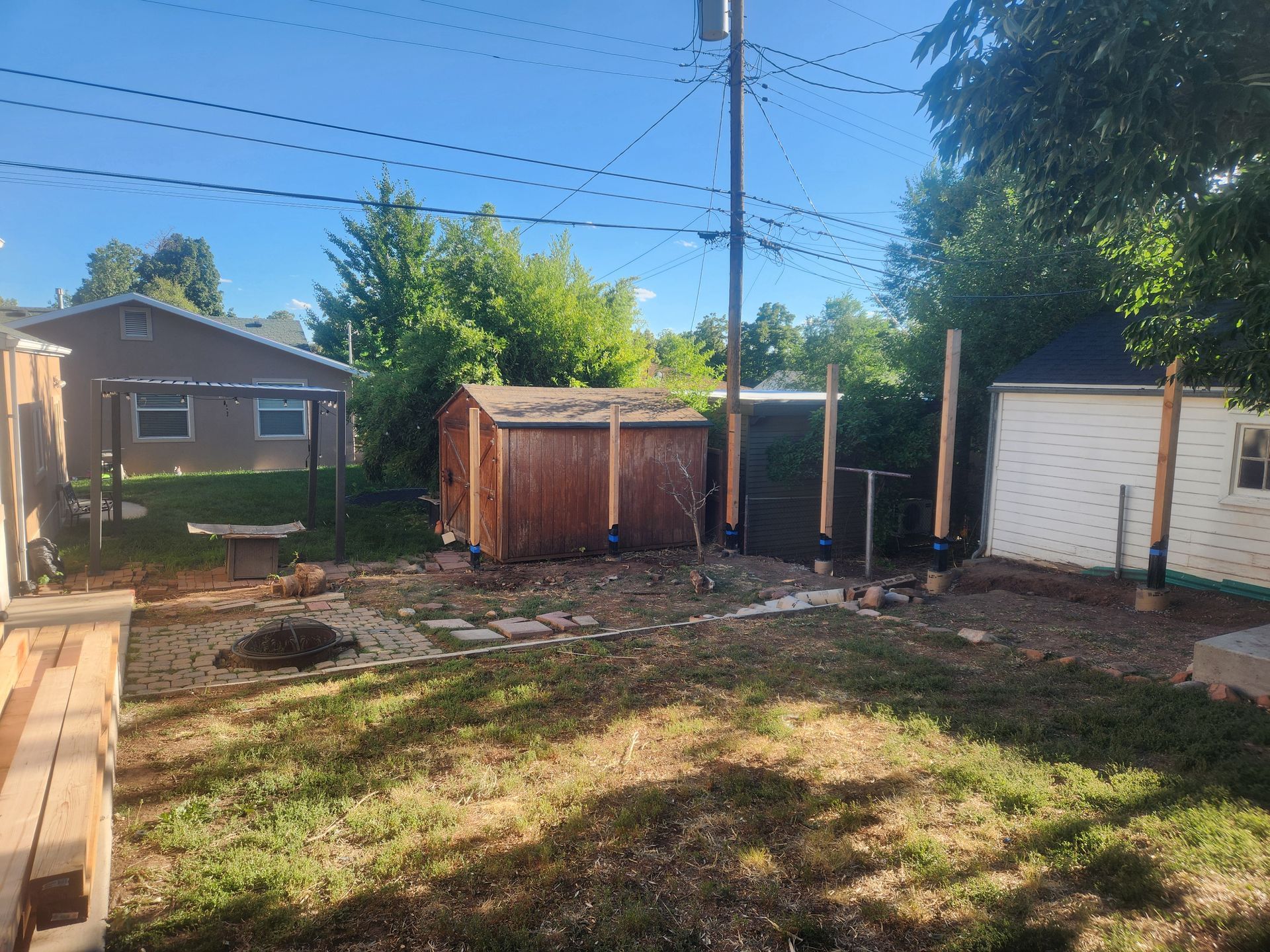 Backyard with a shed, utility poles, and patchy grass on a sunny day