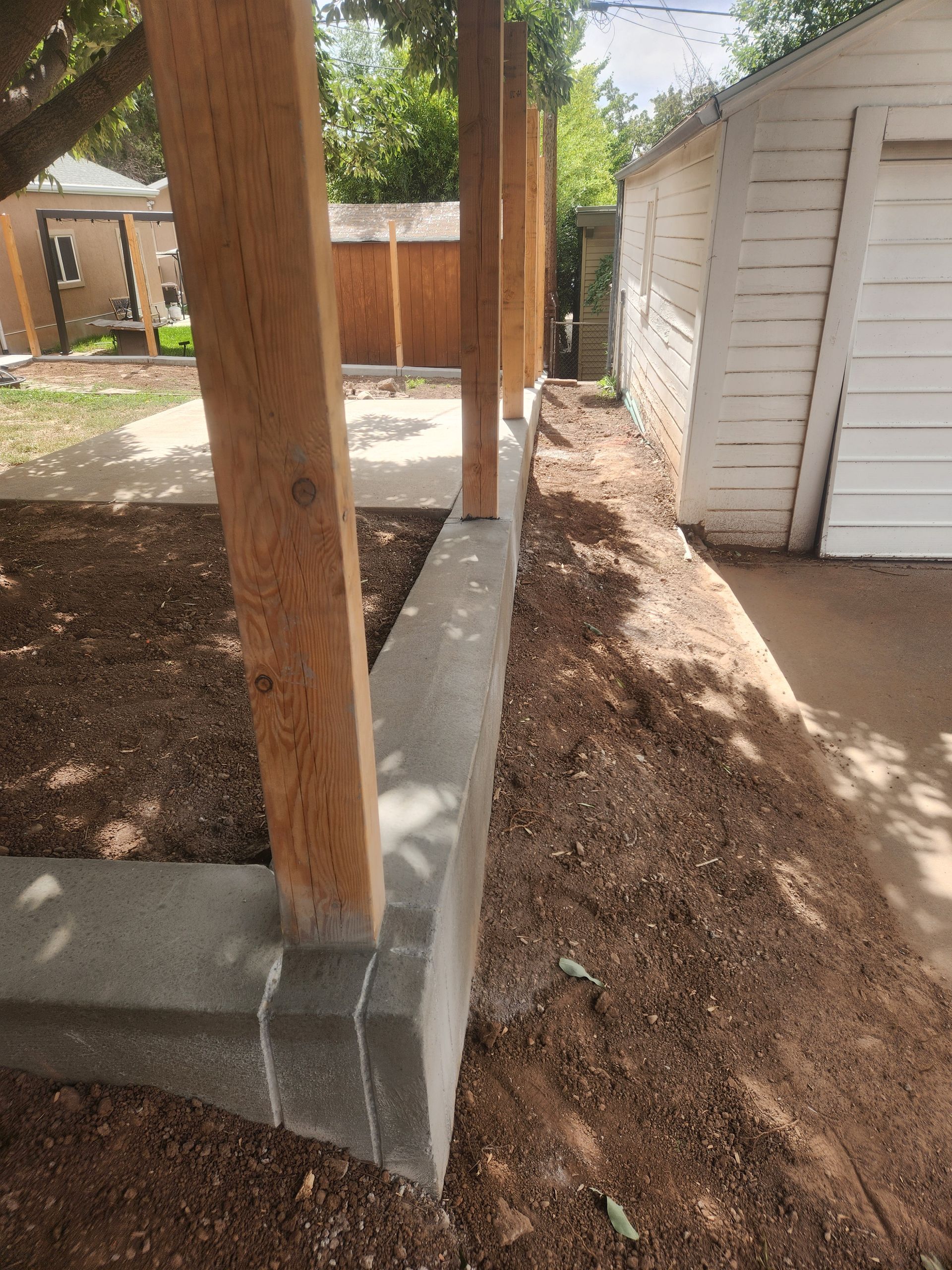Wooden porch posts on concrete footings beside a white garage in a dirt backyard.