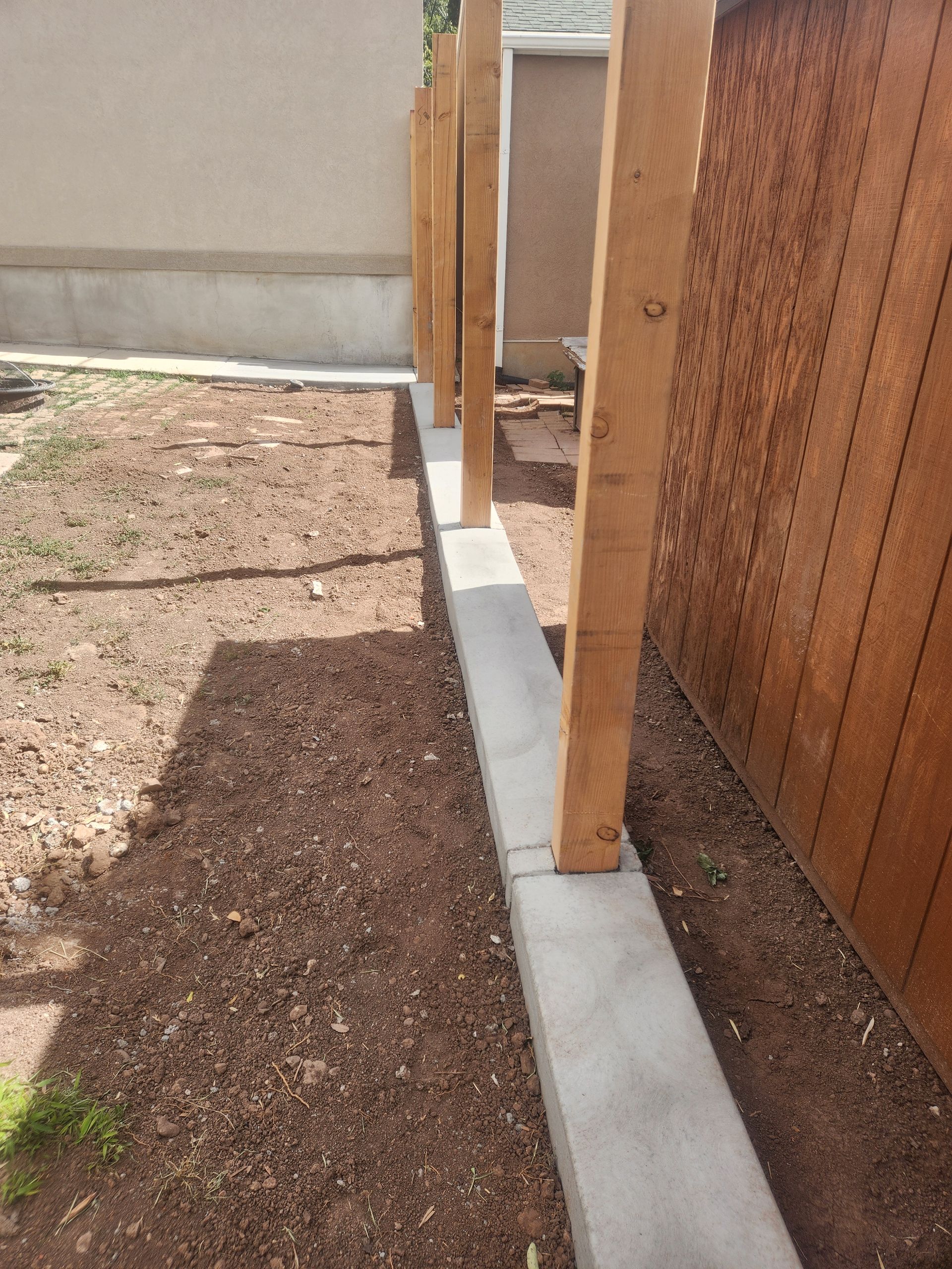 Backyard fence posts set along a narrow concrete border beside a dirt and gravel path