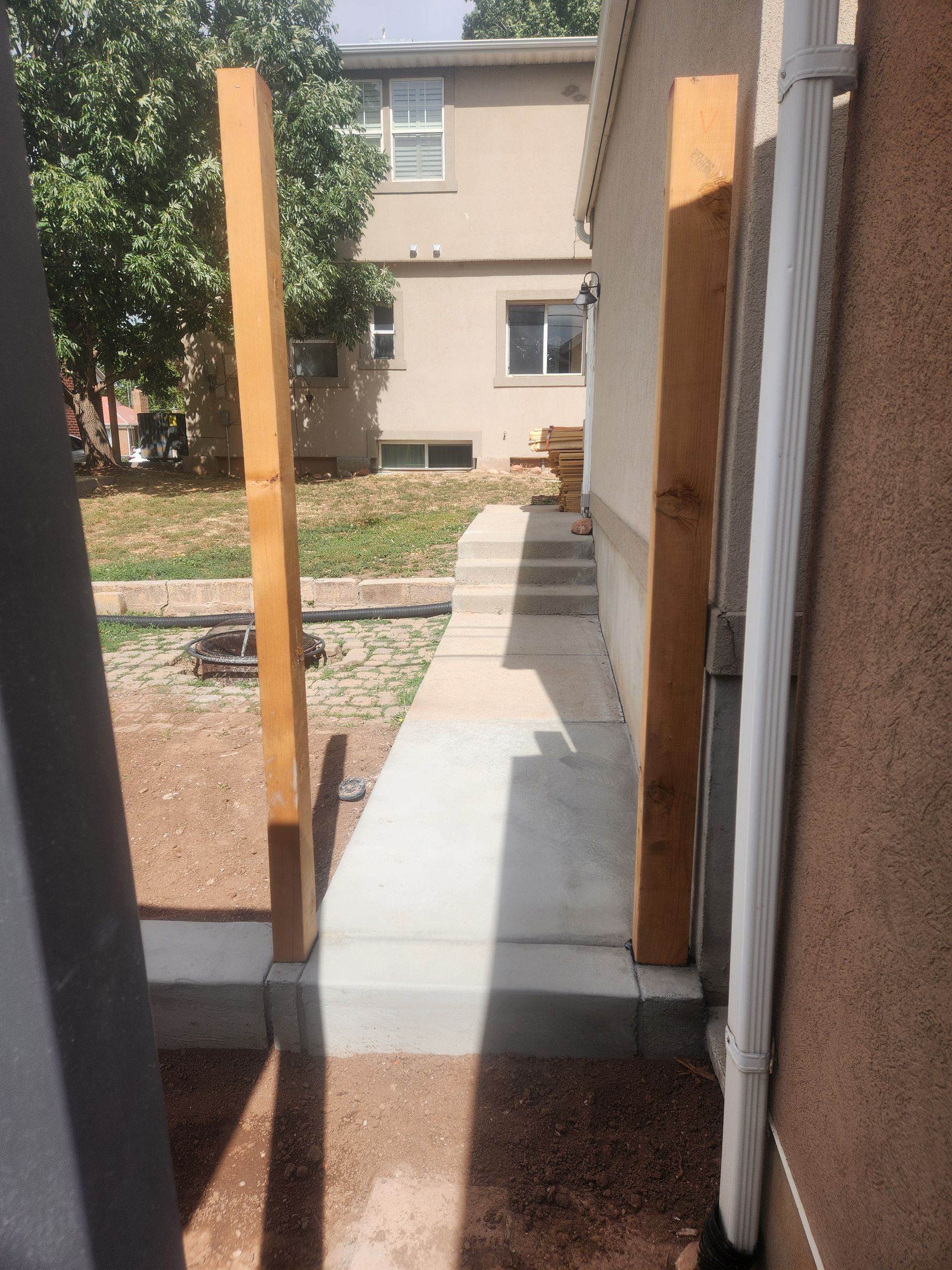 Narrow concrete walkway with wooden posts leading toward a beige building entrance.