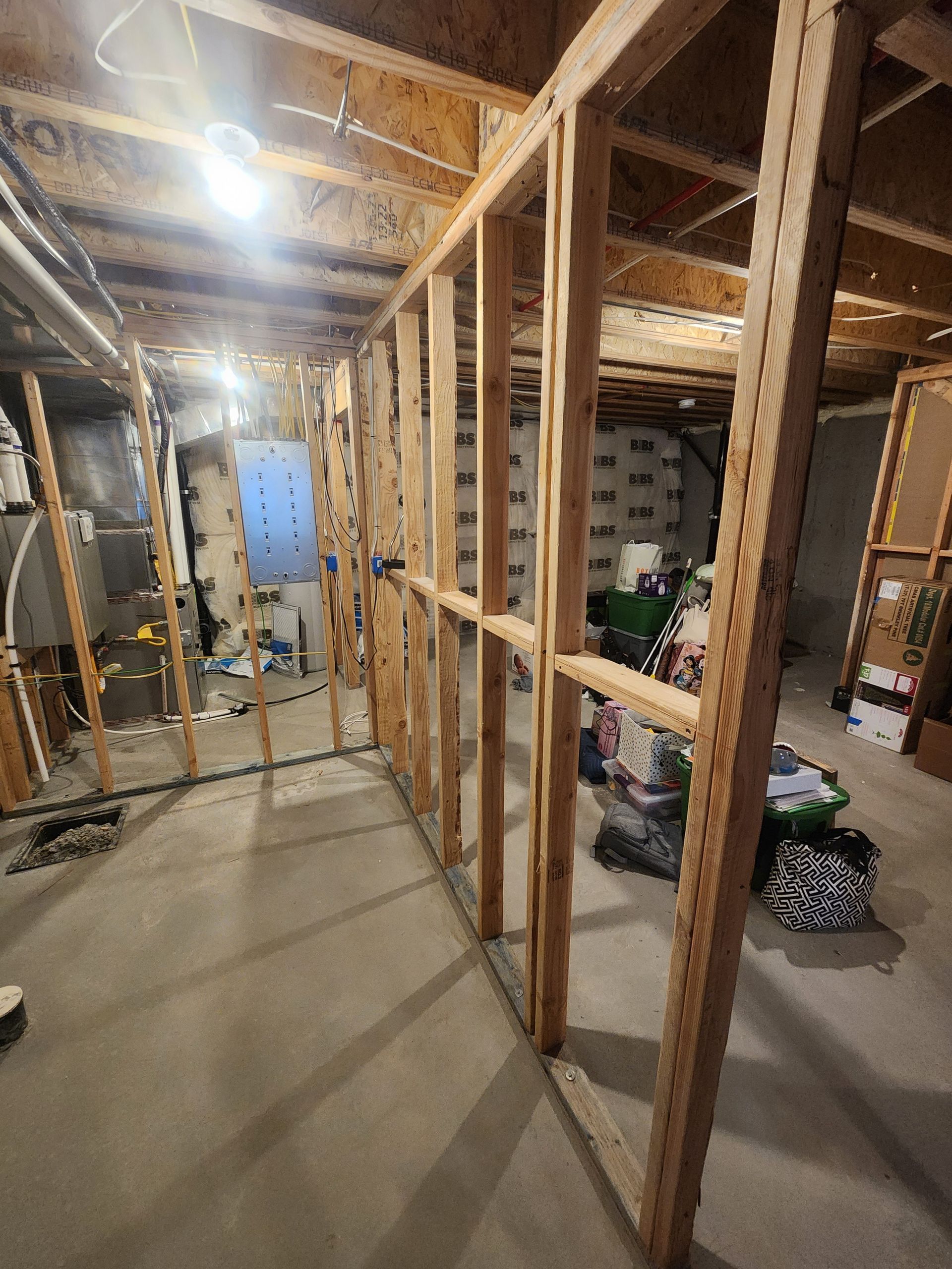 Unfinished basement with exposed wooden framing, concrete floor, and storage items along the right side.