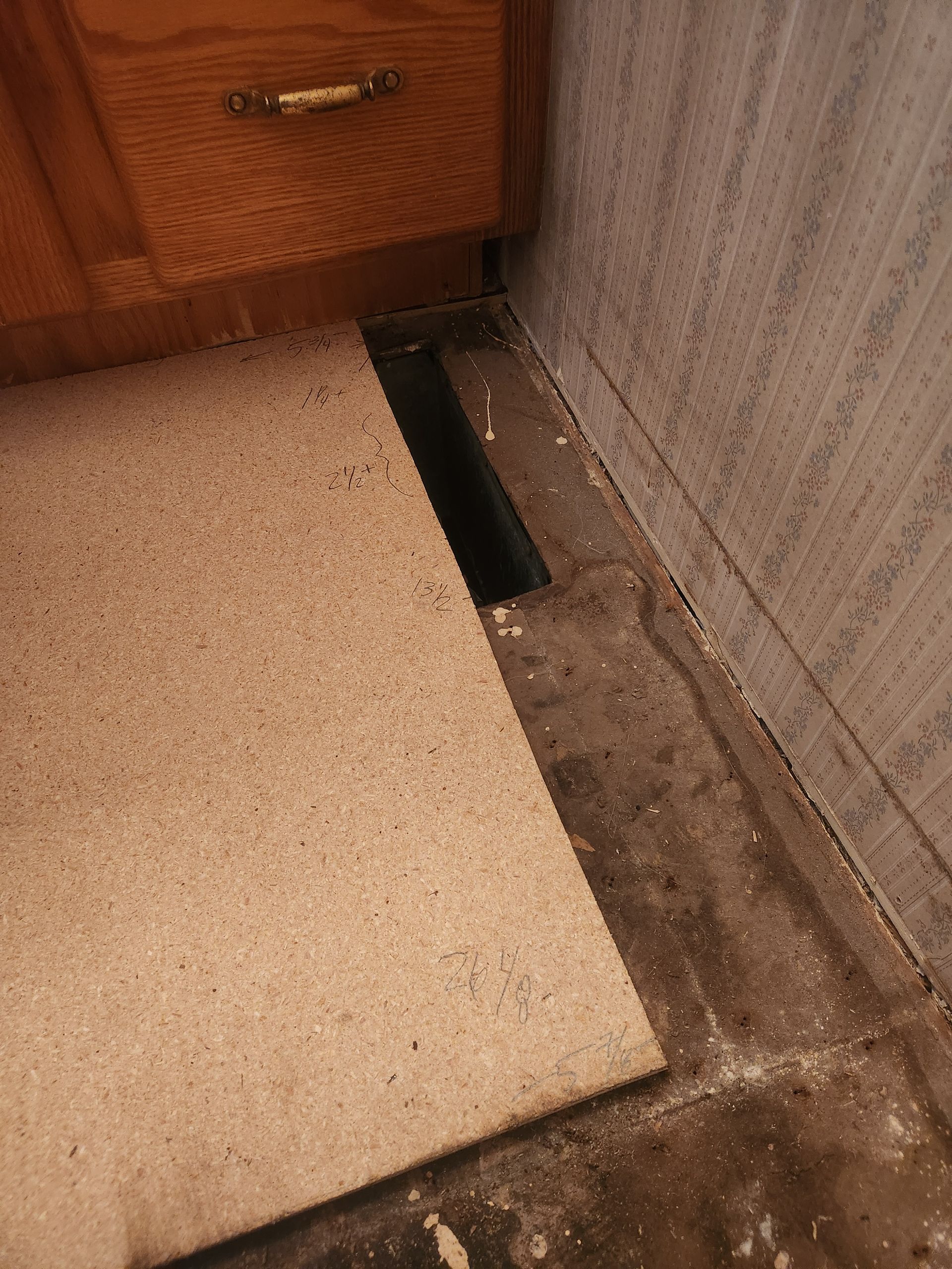 Carpet lifted in a corner, exposing a floor gap beside a wooden cabinet and wall.