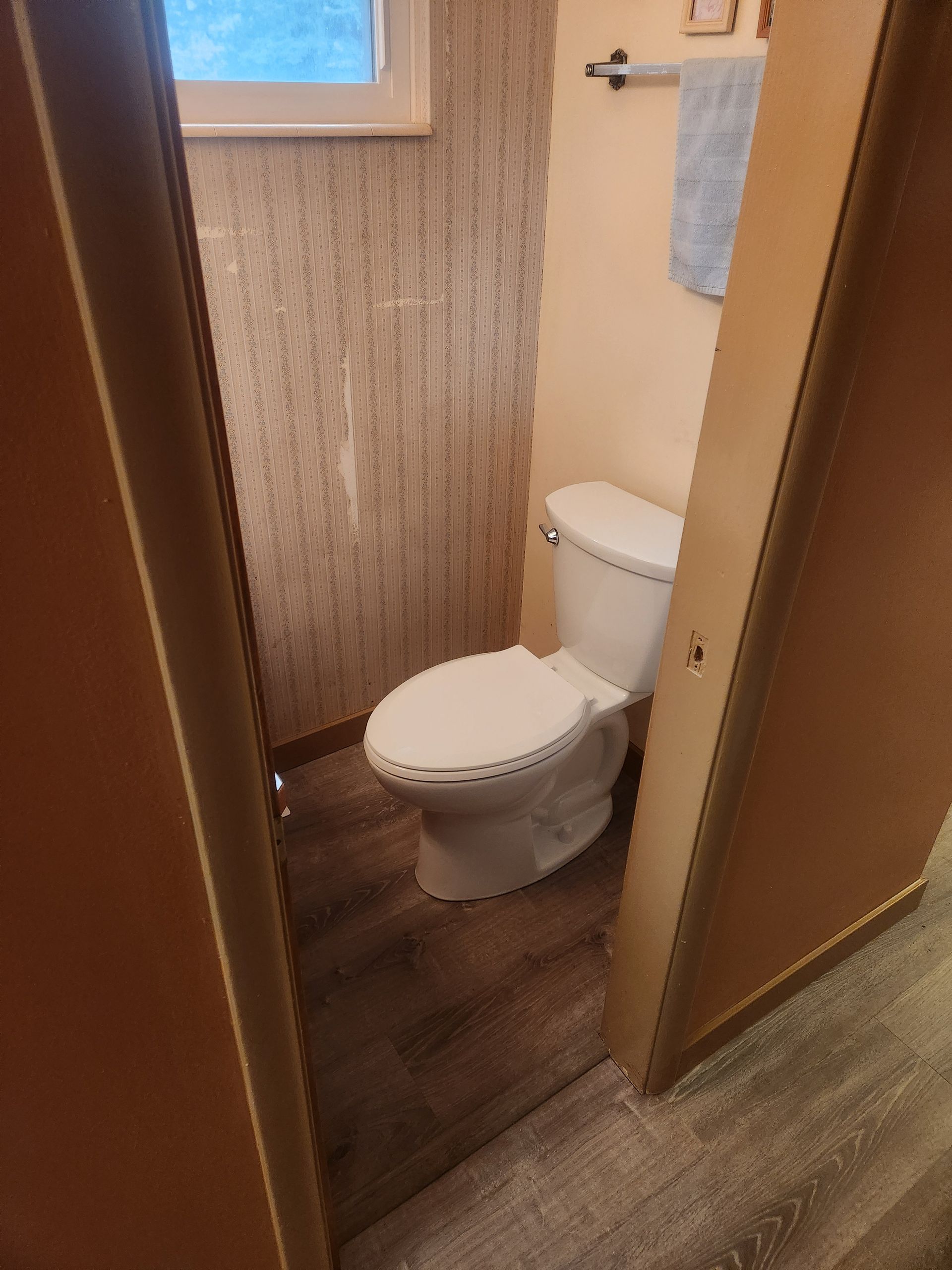Small bathroom with a toilet in a narrow stall, viewed through a doorway.