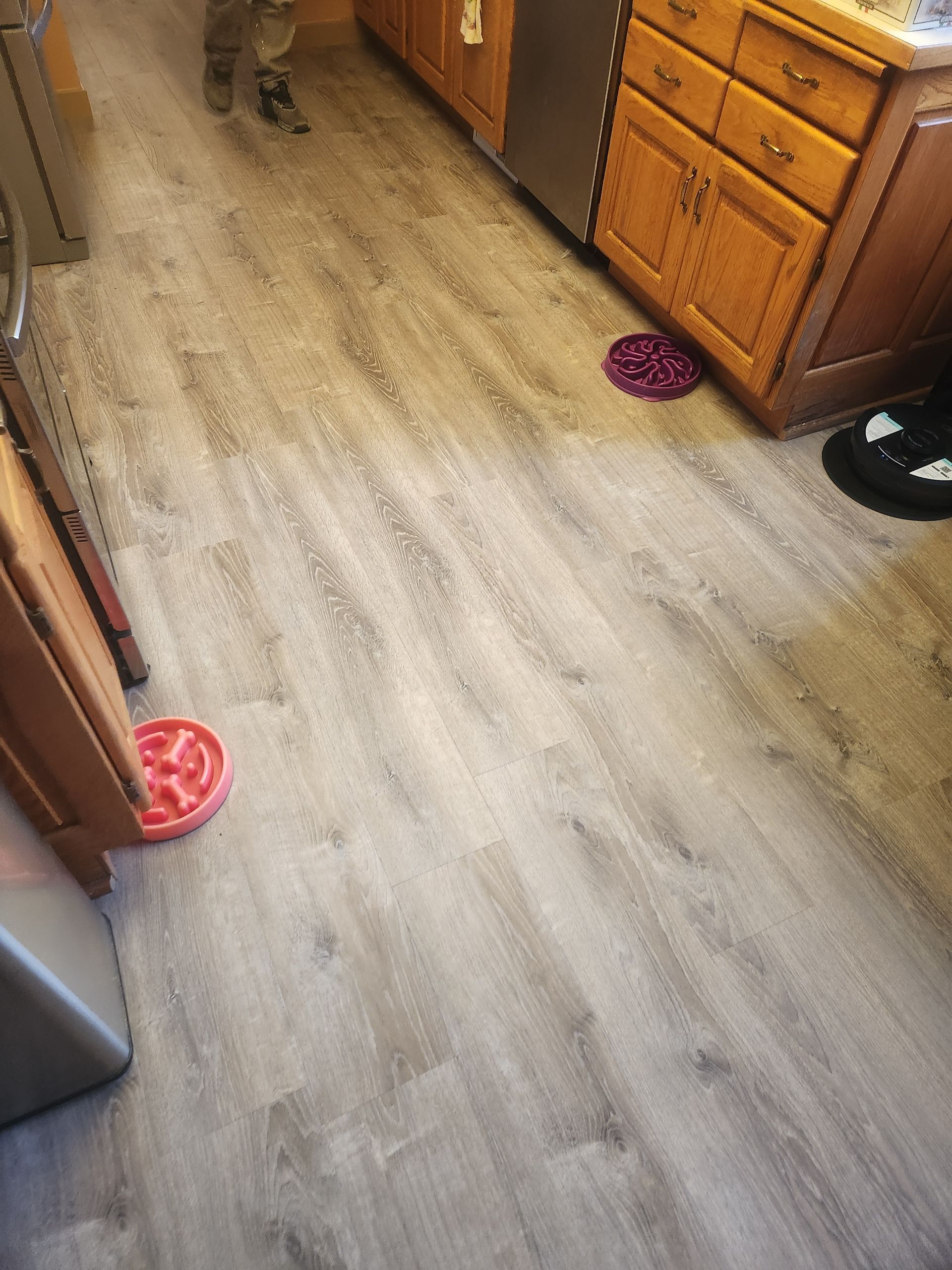 Kitchen floor with gray wood-look planks, wooden cabinets, and pet bowls near the counters.