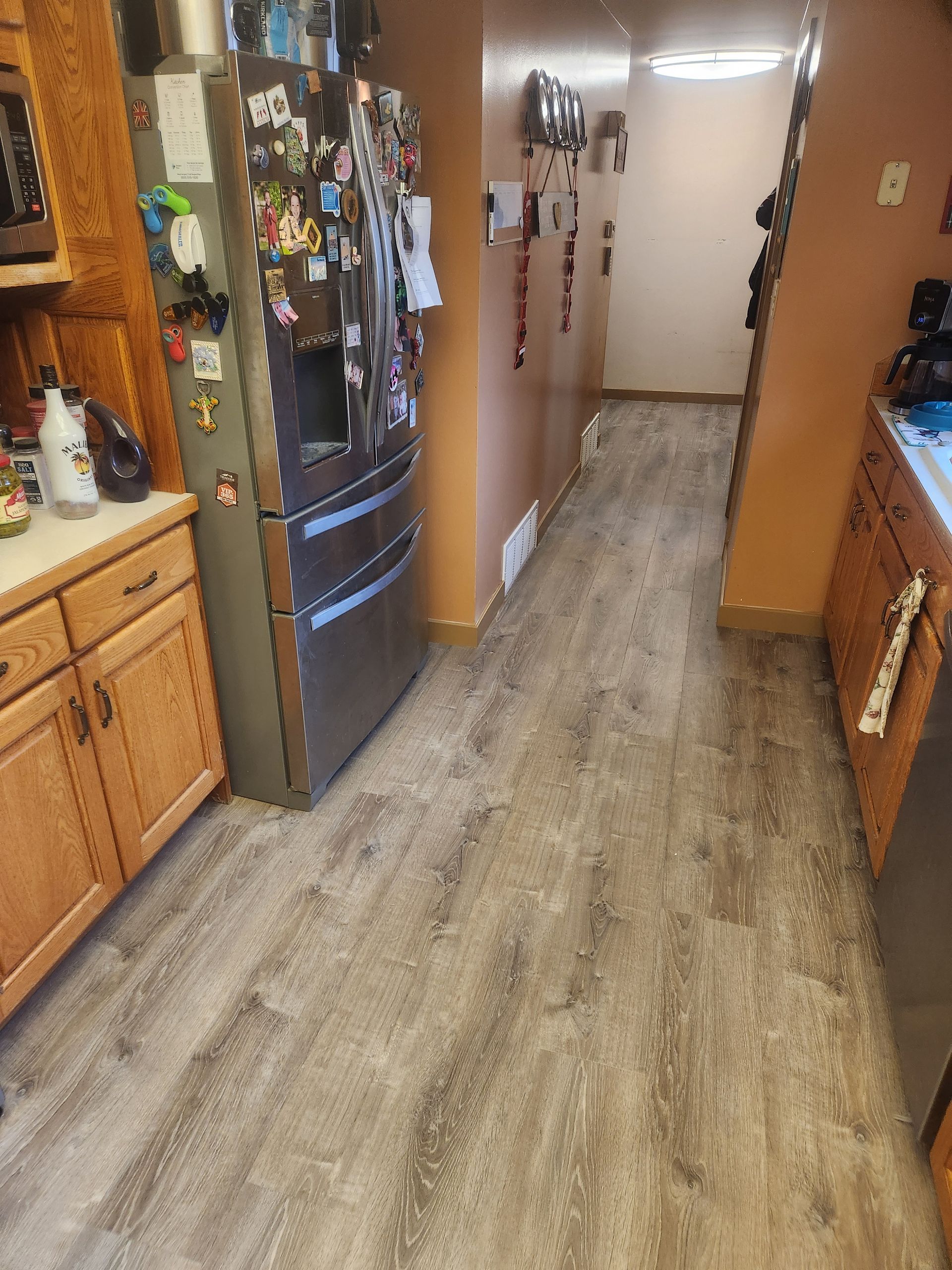 Narrow kitchen hallway with wood cabinets, black refrigerator, and light wood flooring.