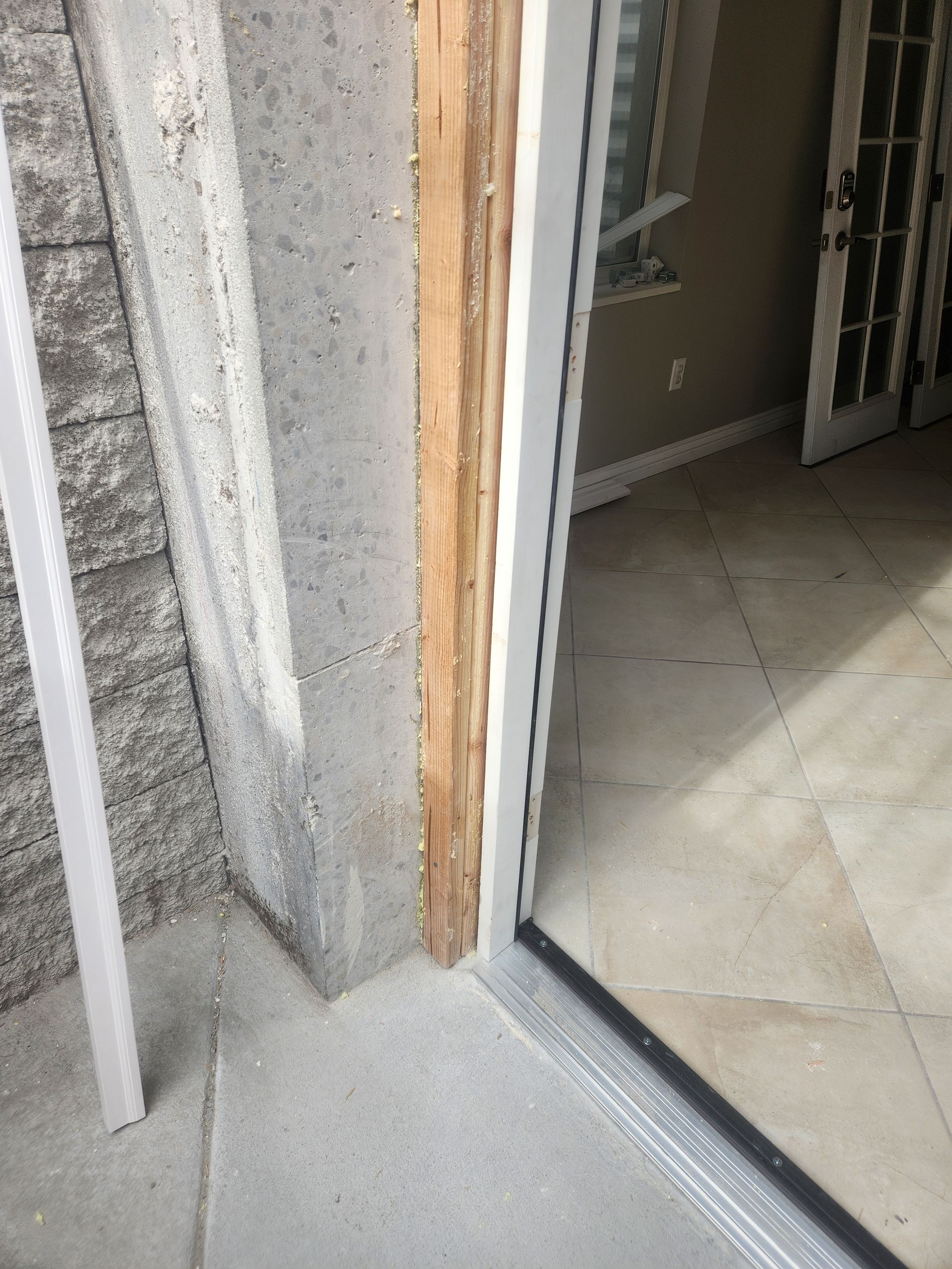 Open doorway with threshold strip between a rough concrete wall and a tiled interior floor