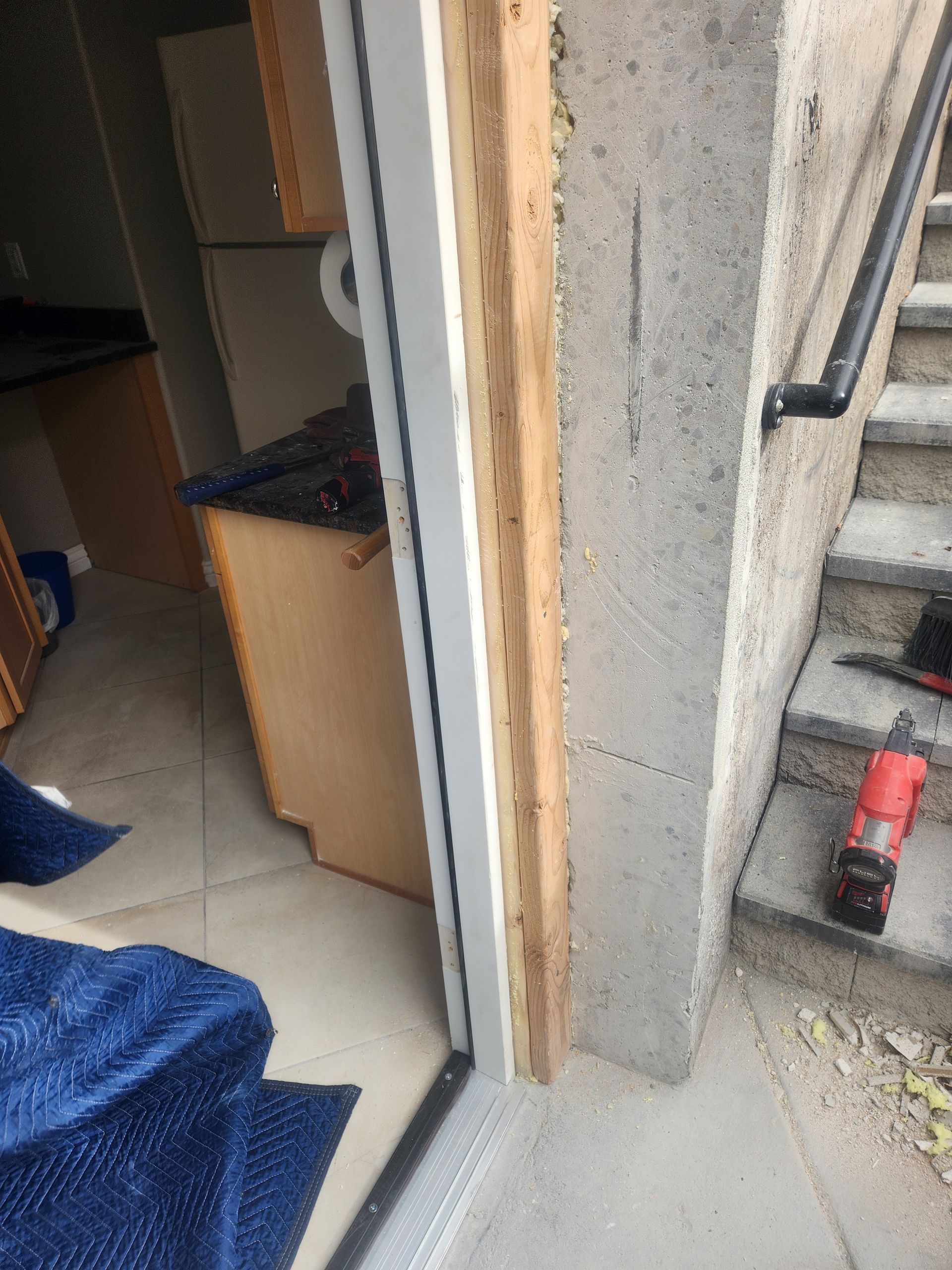 Open doorway to a room with a desk, beside concrete stairs and a red cordless drill on the floor.