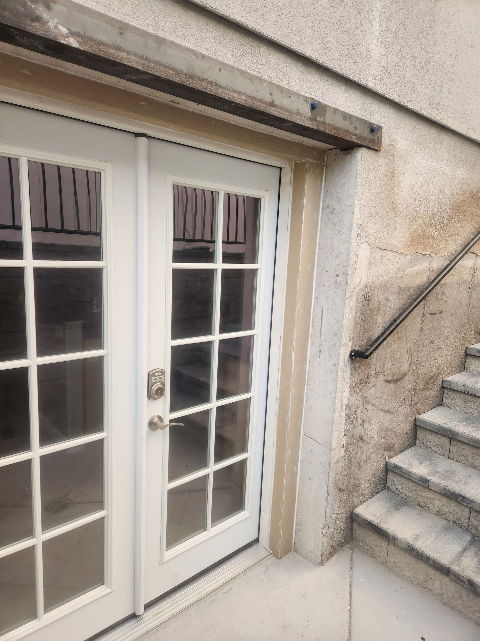 White French doors beside concrete steps against a beige stucco wall