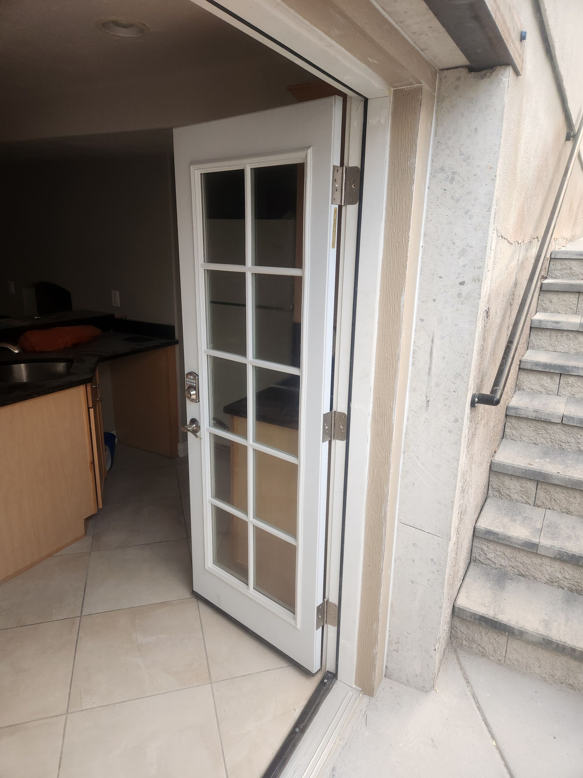 Open white French door beside concrete stairs, leading into a tiled interior.