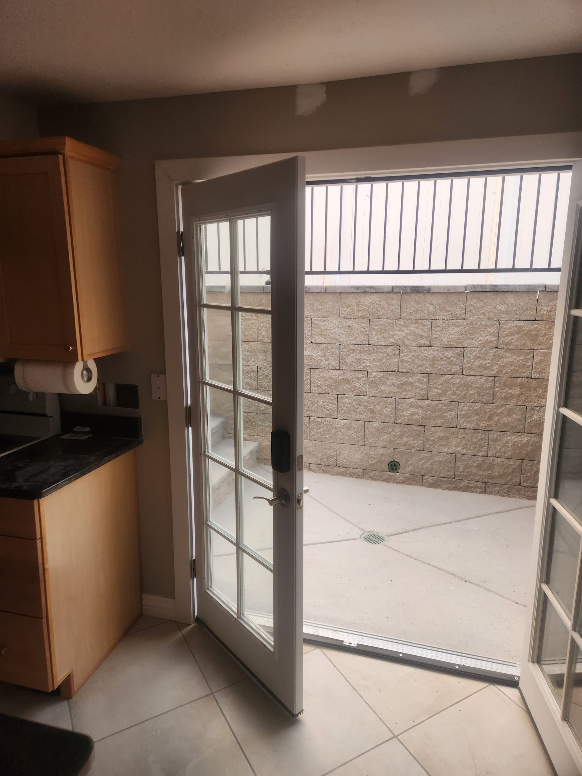 Kitchen interior with open glass door leading to a small tiled patio and stone wall outside