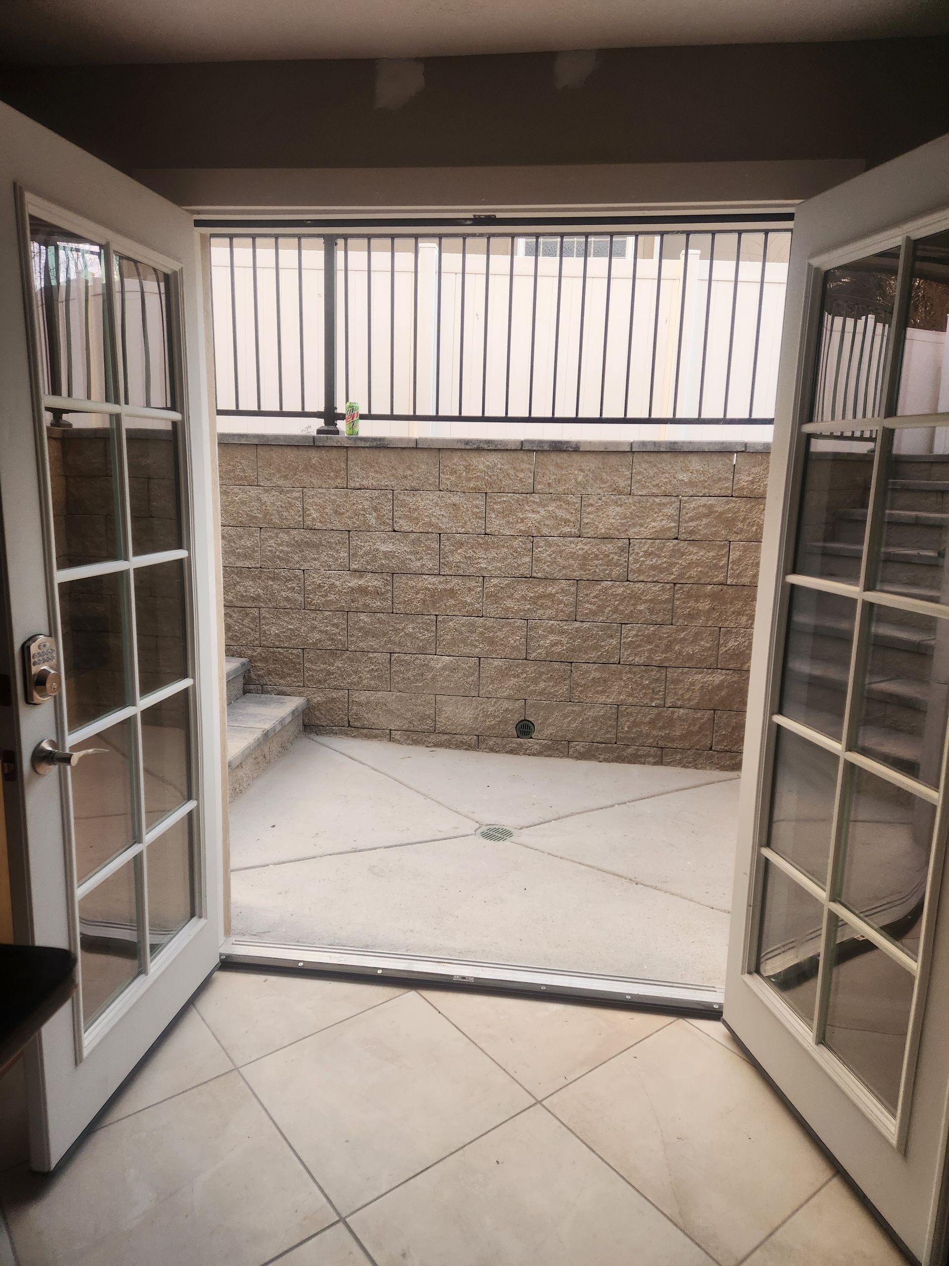 Open double glass doors to a tiled patio with a brick wall and metal railing.