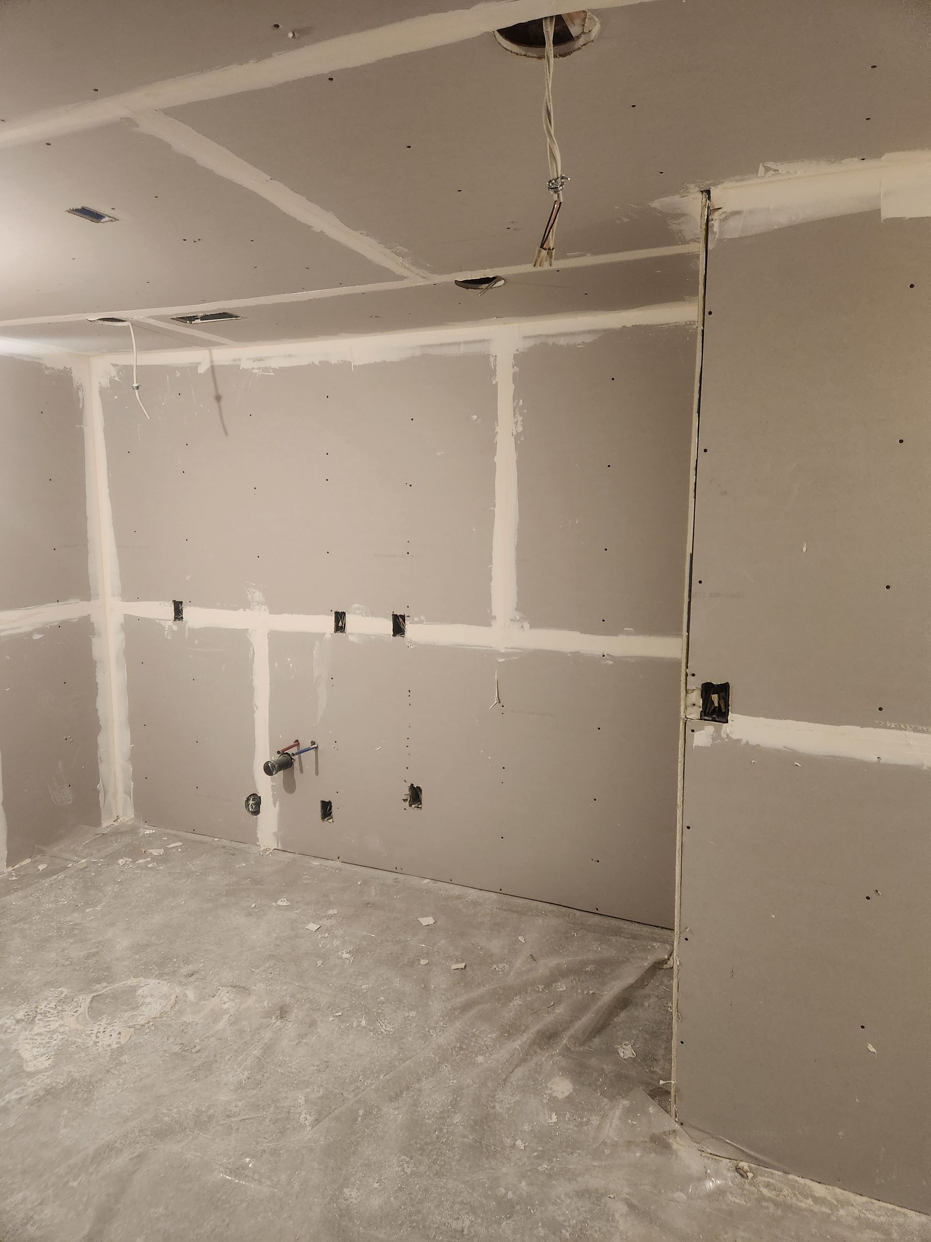 Unfinished drywall room with taped seams, exposed wiring, and dusty concrete floor