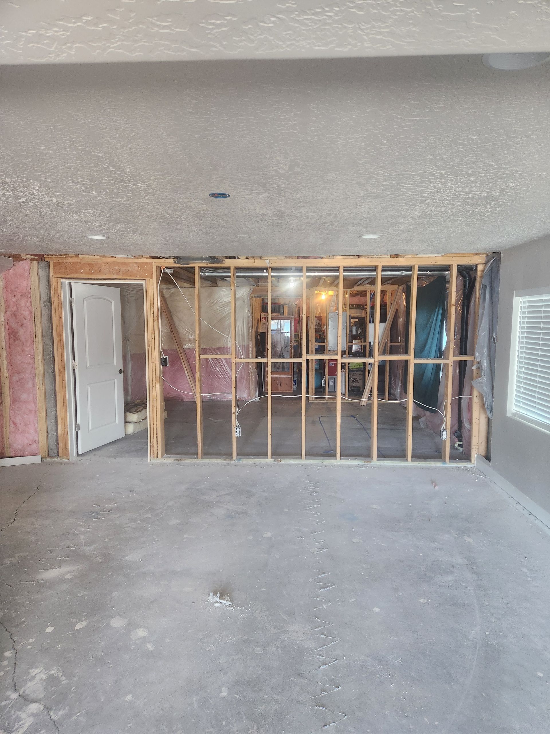 Partially demolished room with exposed wooden studs, pink insulation, and a doorway opening to another room.