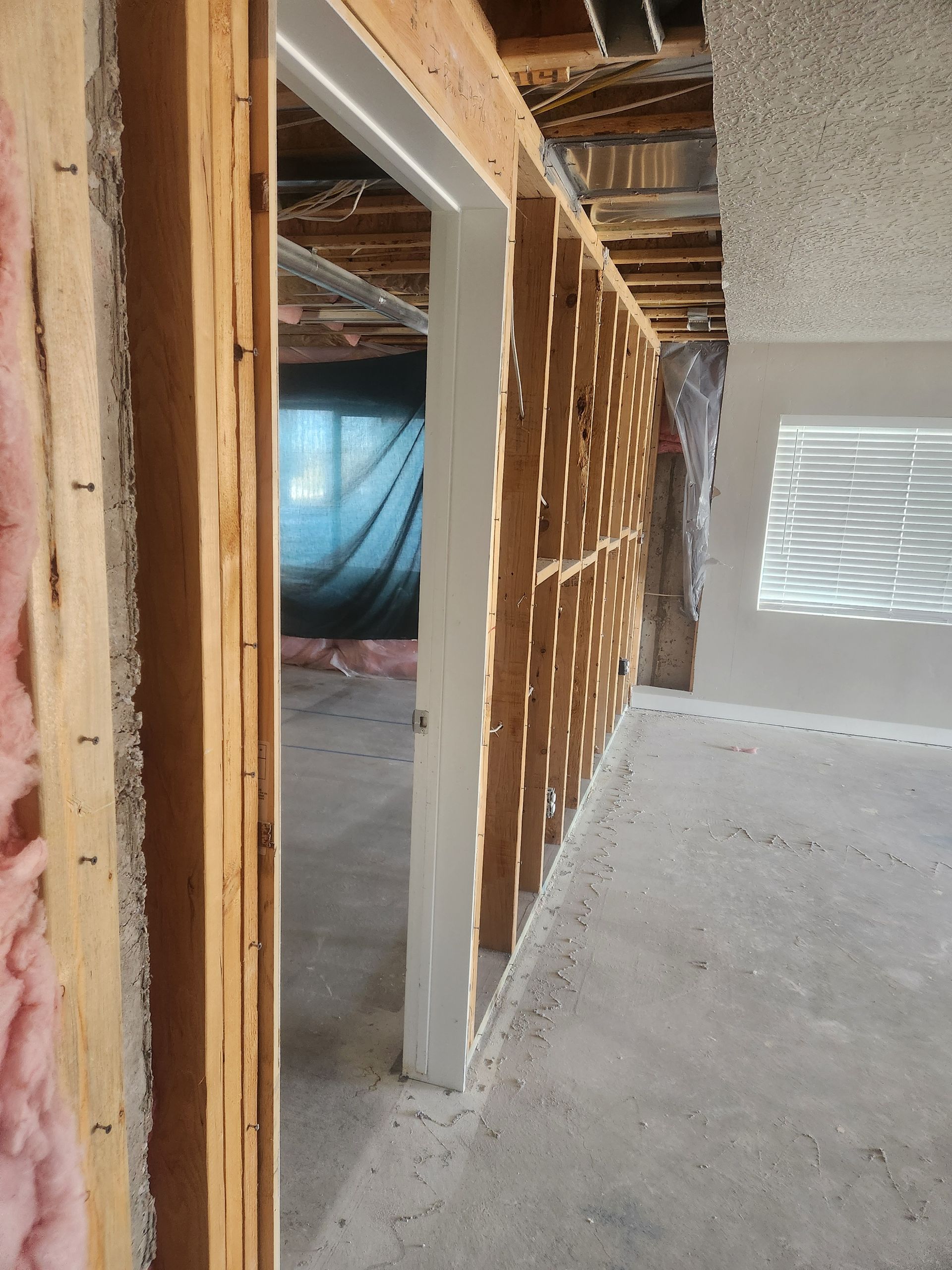 Interior construction site with unfinished wall framing, exposed insulation, and a white vented panel.